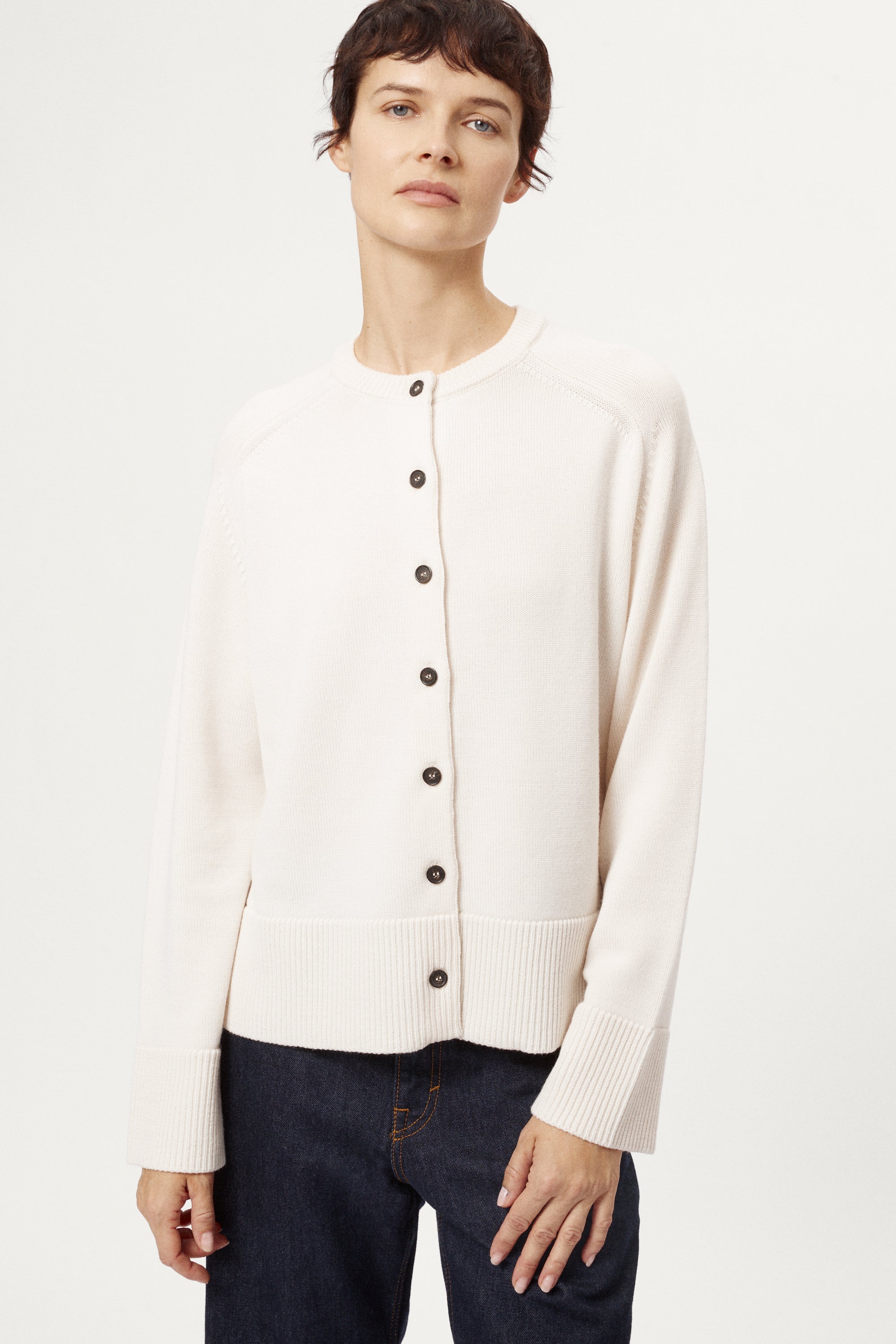Person wearing a cream cardigan with black buttons on a white background