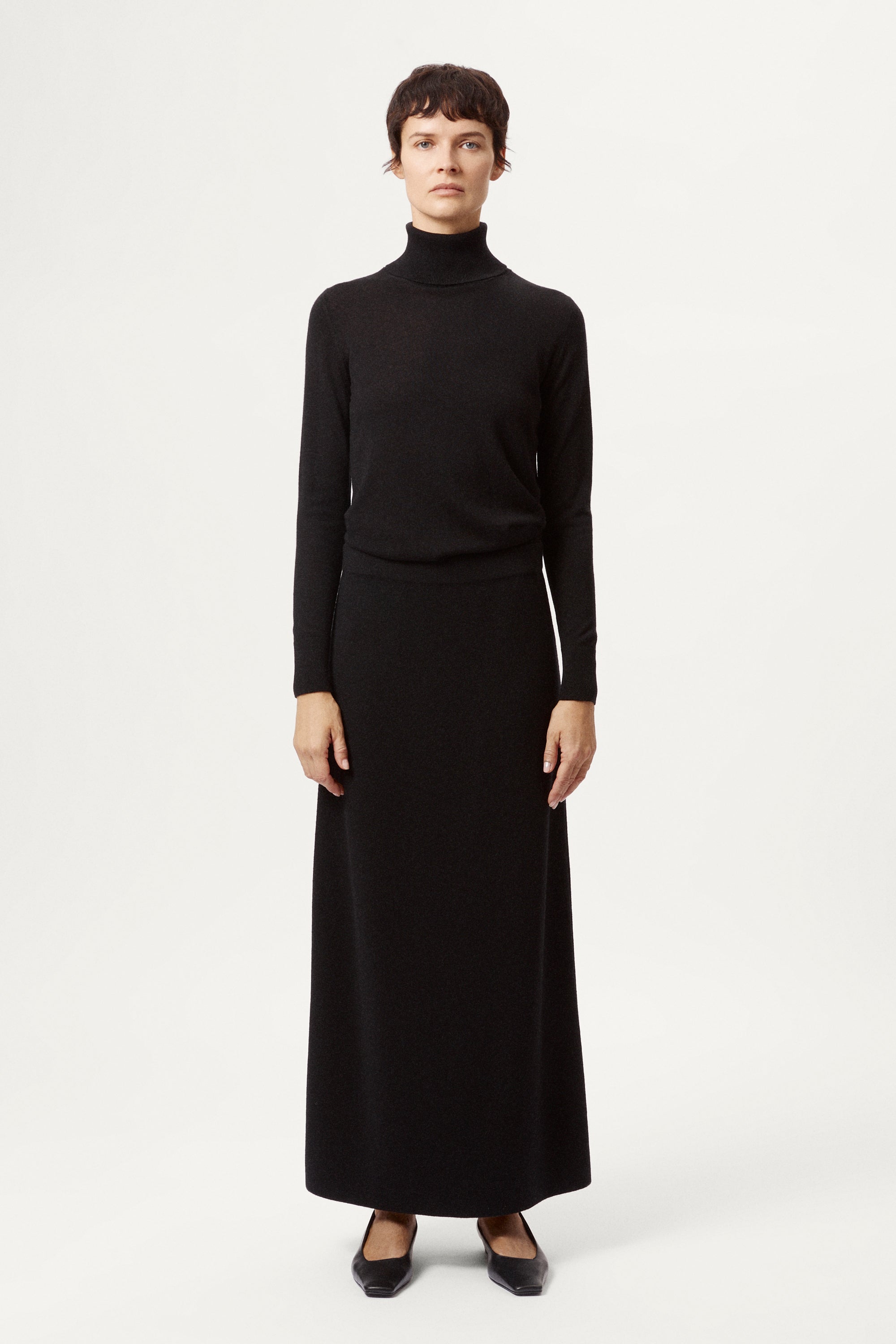 Person wearing a black turtleneck and long black skirt on a white background