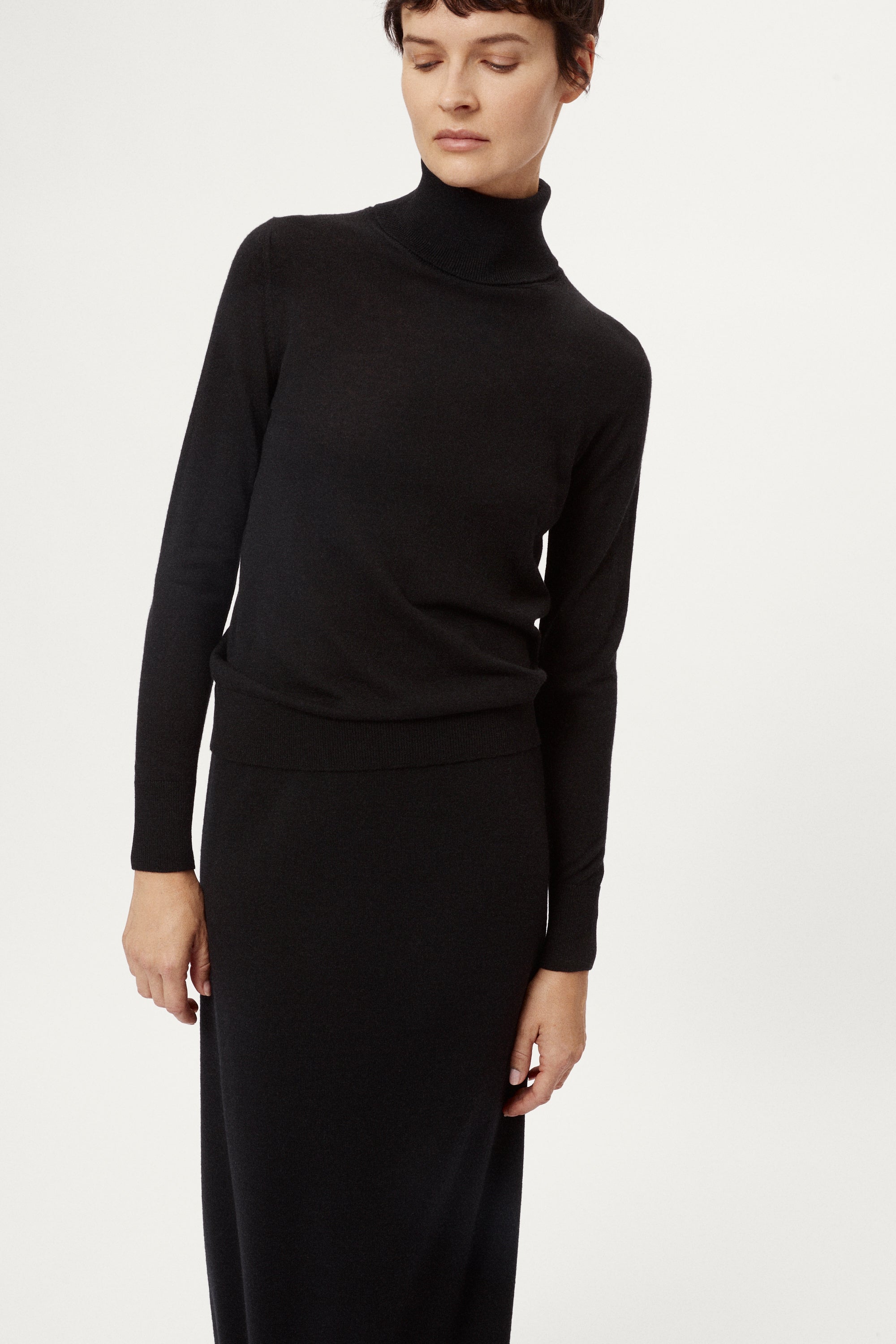 Person wearing a black turtleneck and long black skirt on a white background