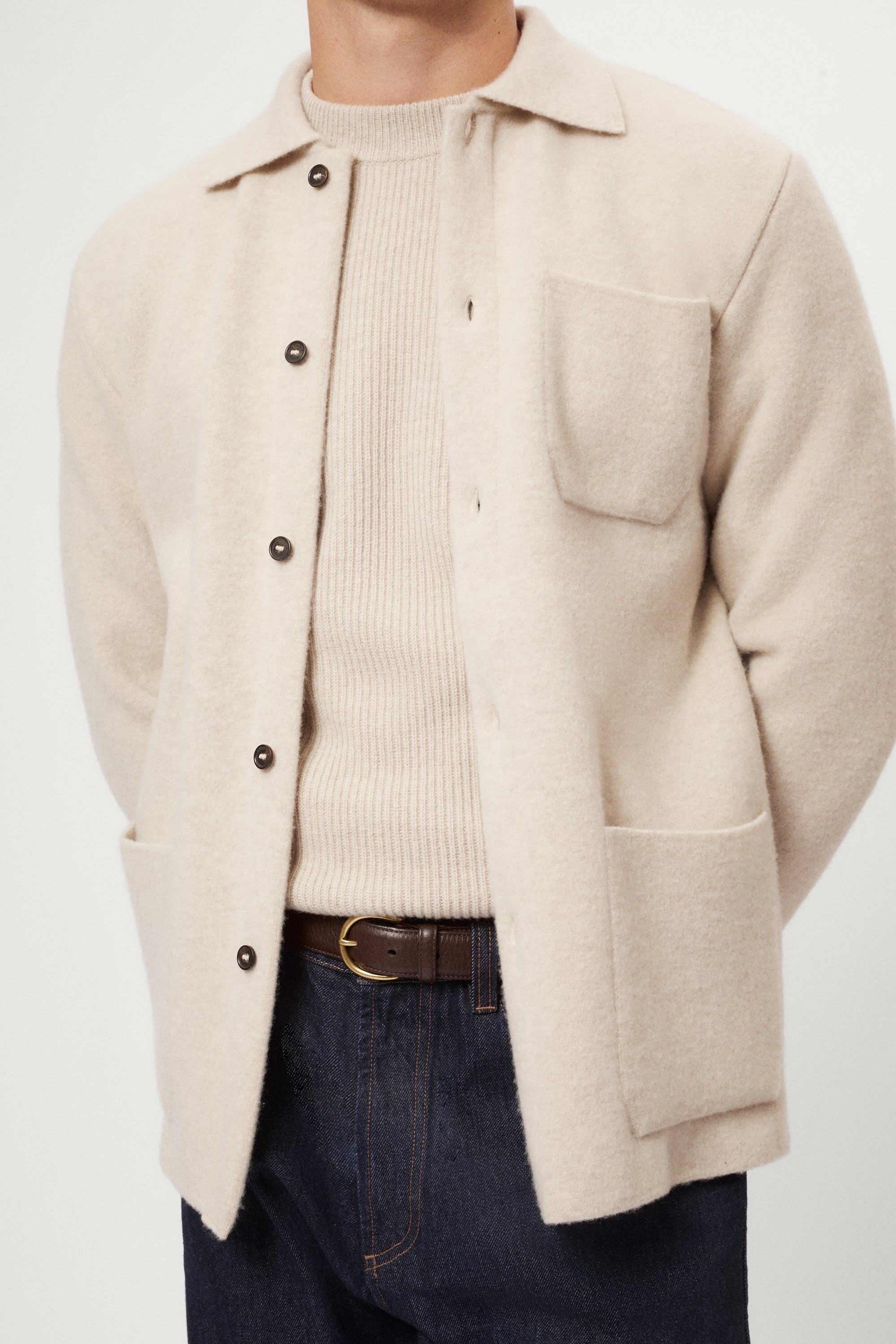 Person wearing a beige Boiled Wool Jacket over a knit sweater with a plain background