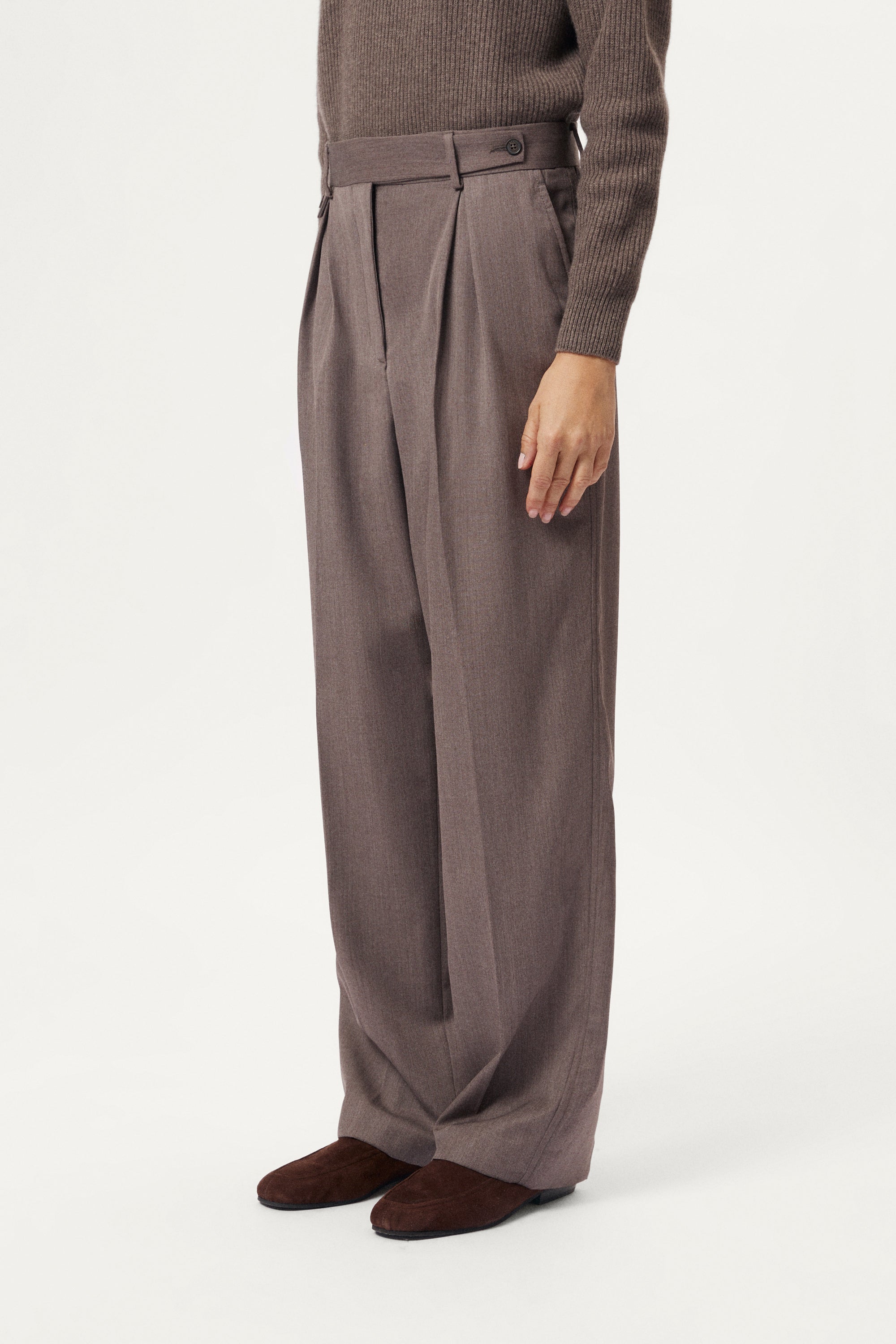 Brown pleated pants worn by a person on a white background
