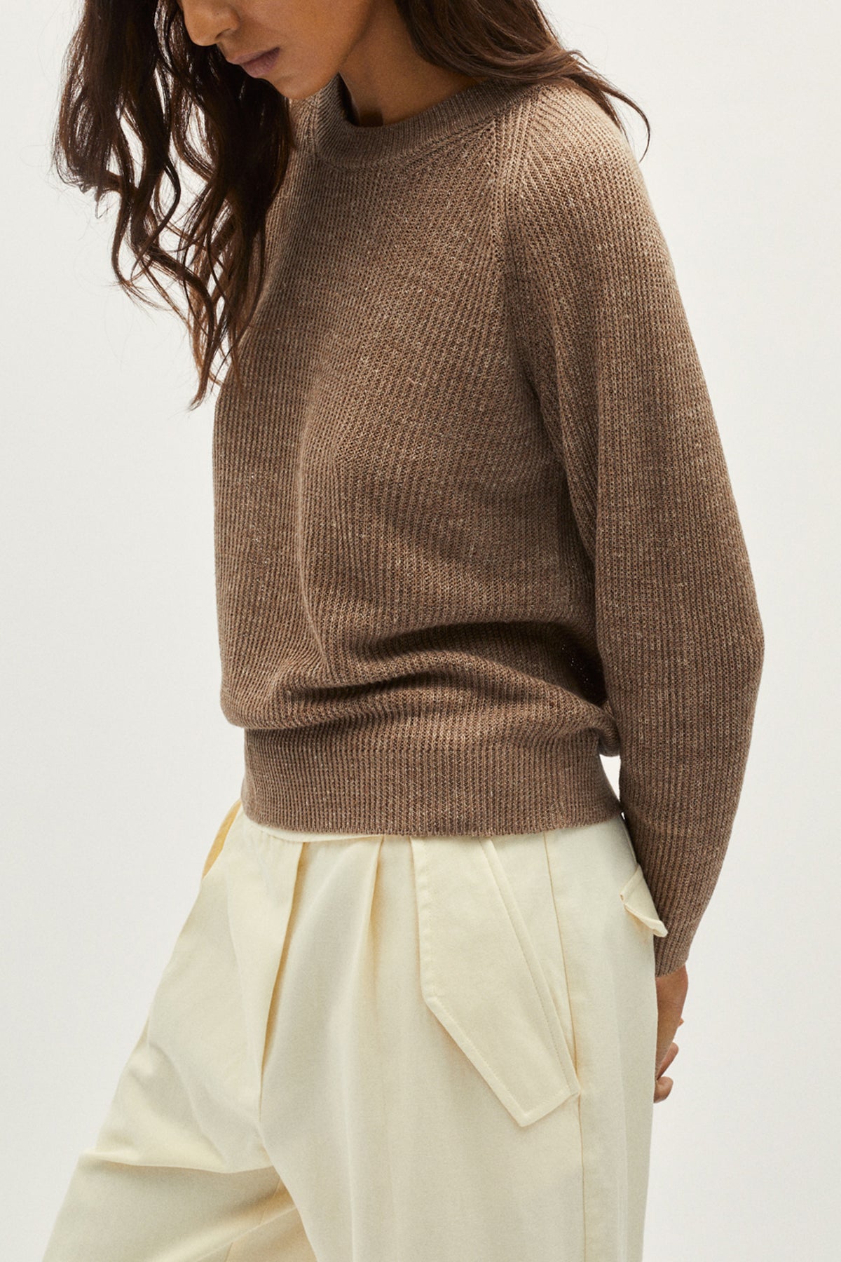 Person wearing a brown sweater and light-colored pants on a white background