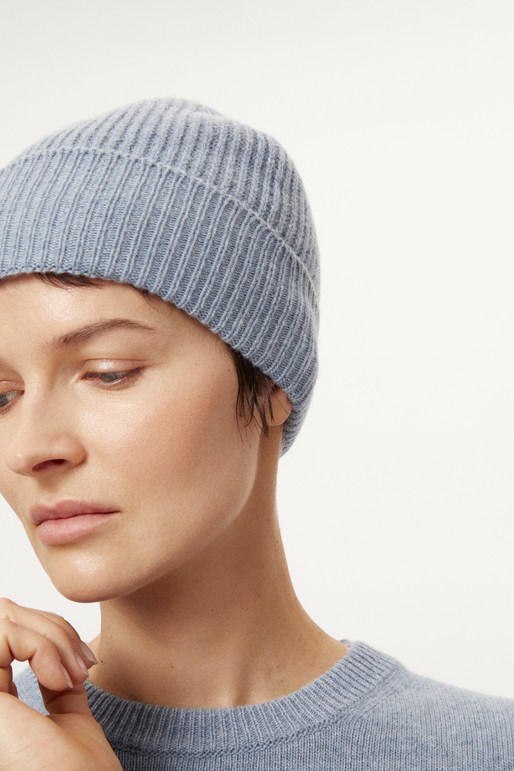 woman wearing a woolen light blue knit beanie and sweater against a white background