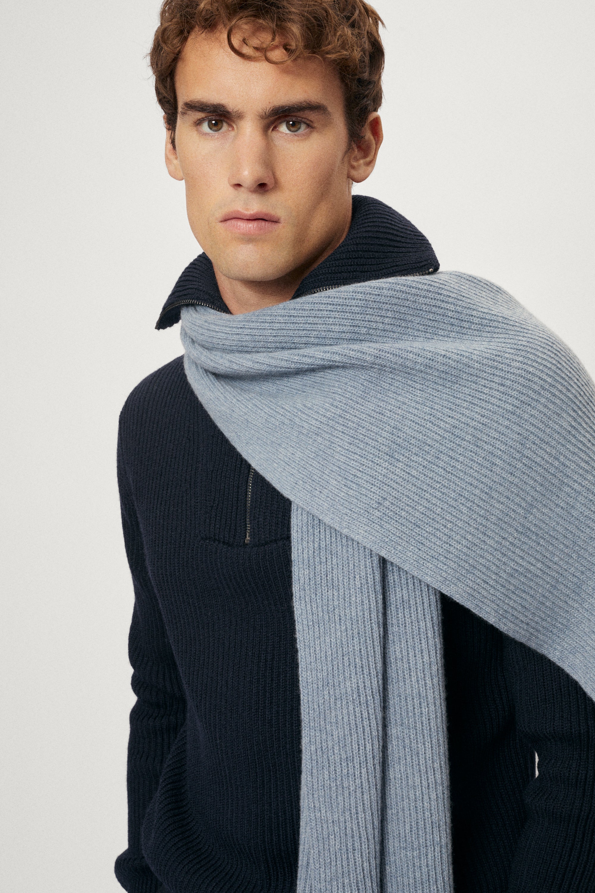 Man wearing a ash blue woolen scarf over his shoulders against a plain background