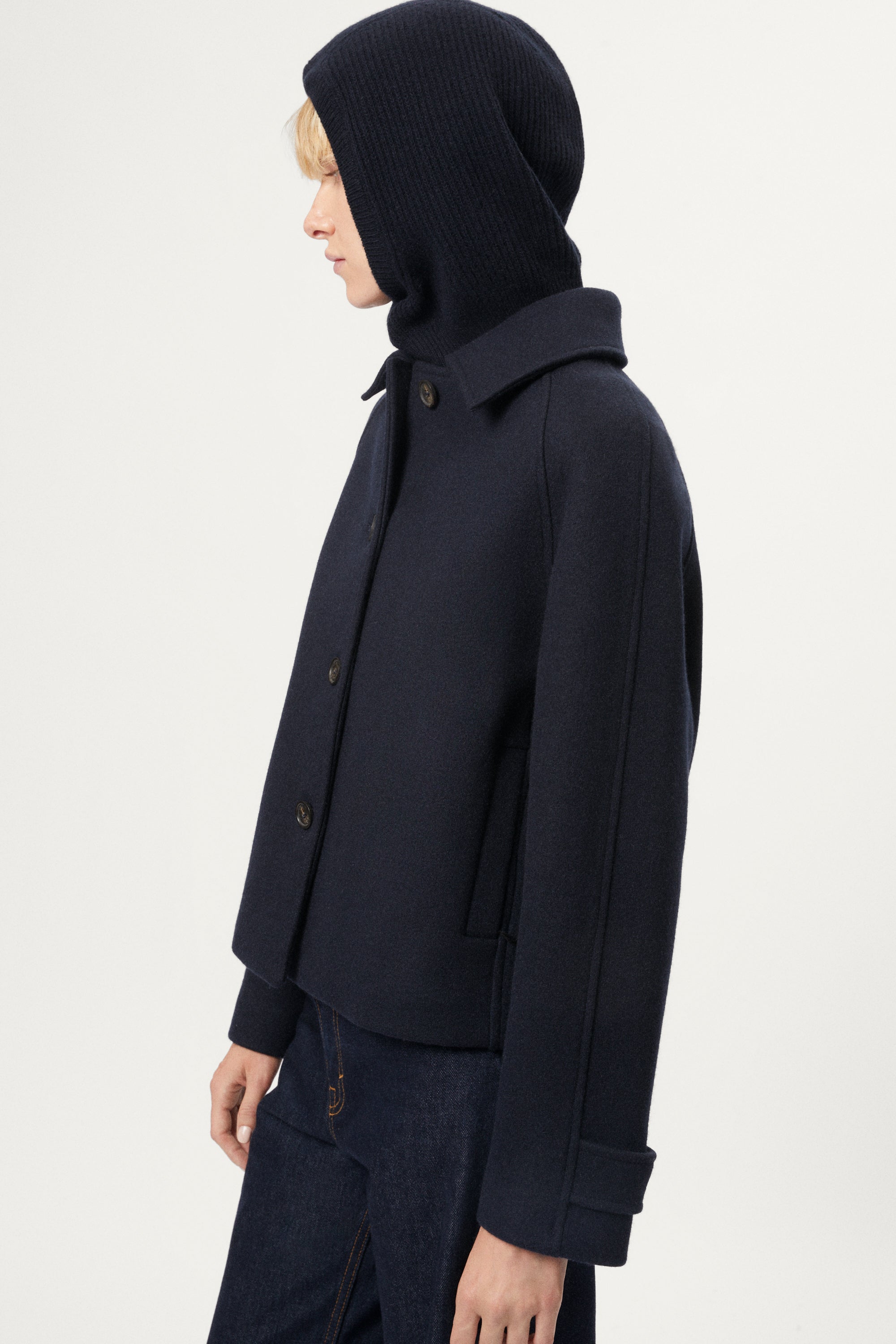 woman wearing a woolen dark blue balaclava jacket on a light gray background