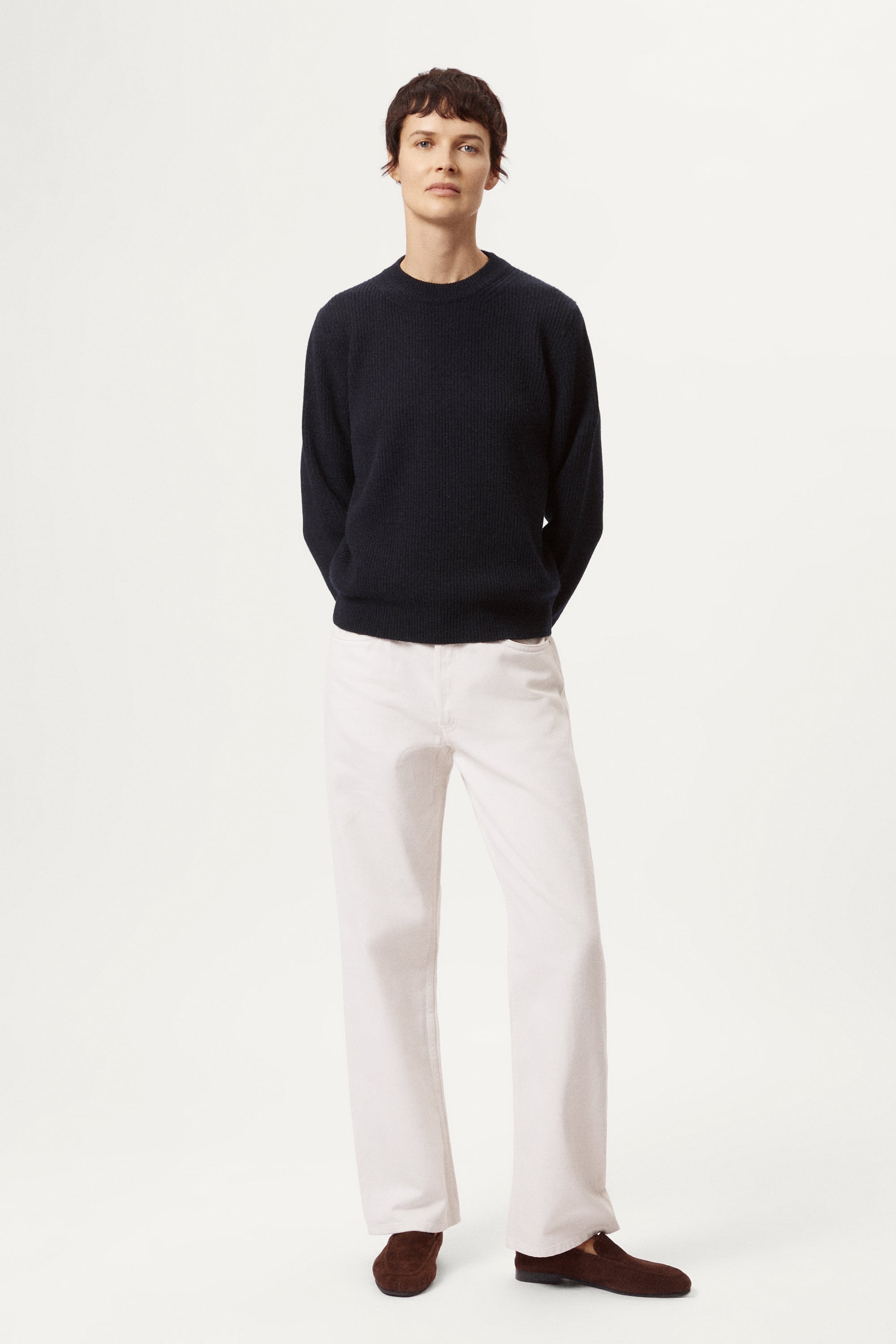 woman wearing a blue navy woolen sweater and white pants against a light background