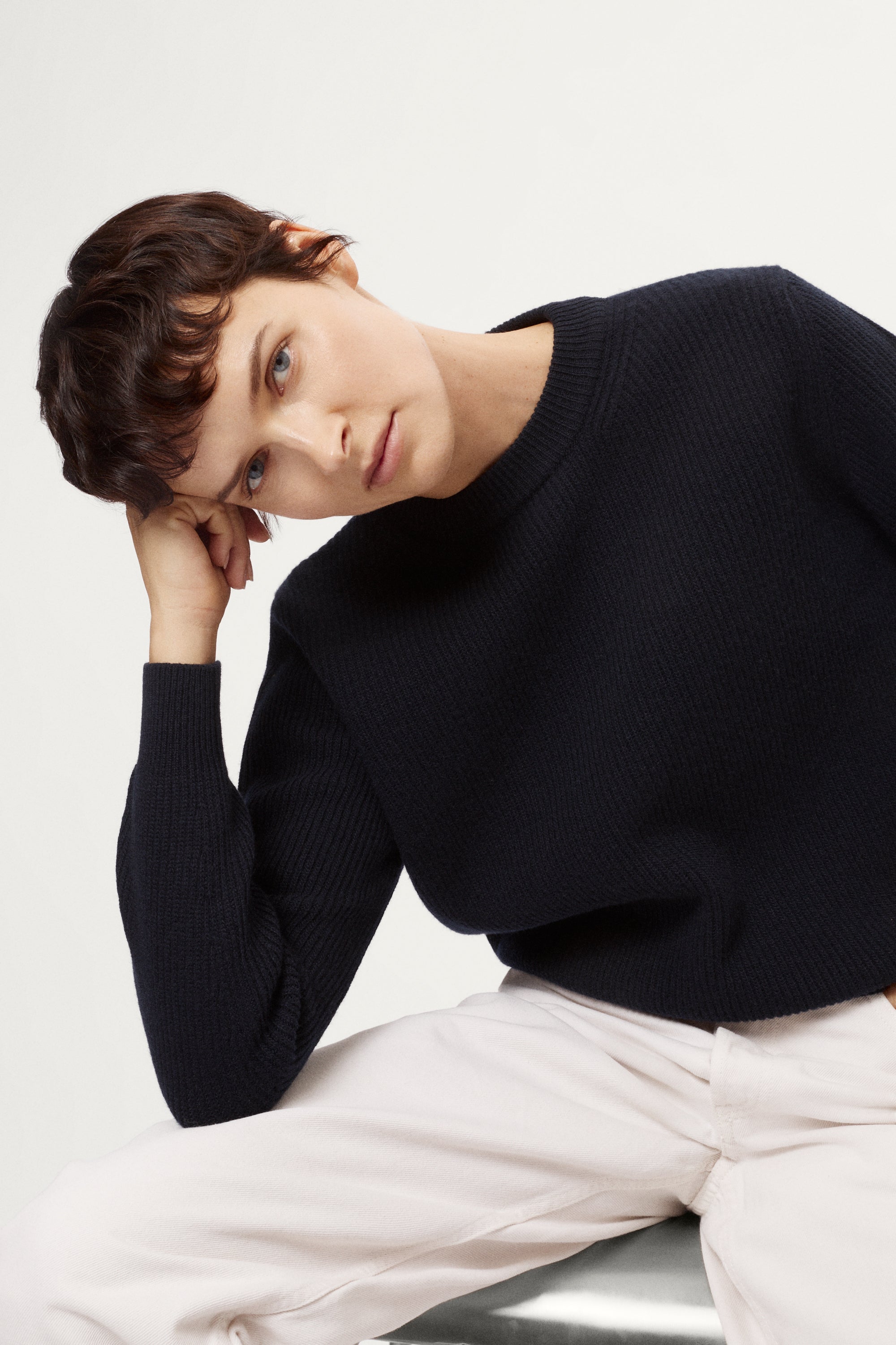 woman wearing a blue navy woolen sweater and white pants against a light background