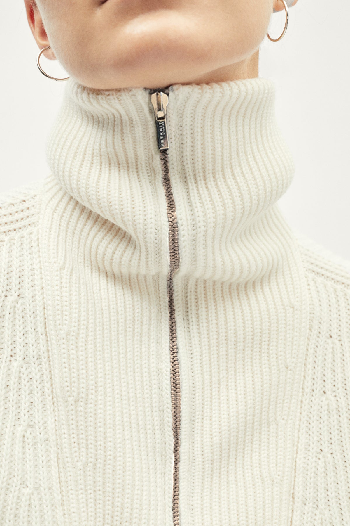 Close-up of a white ribbed knit sweater with a zipper on a plain background