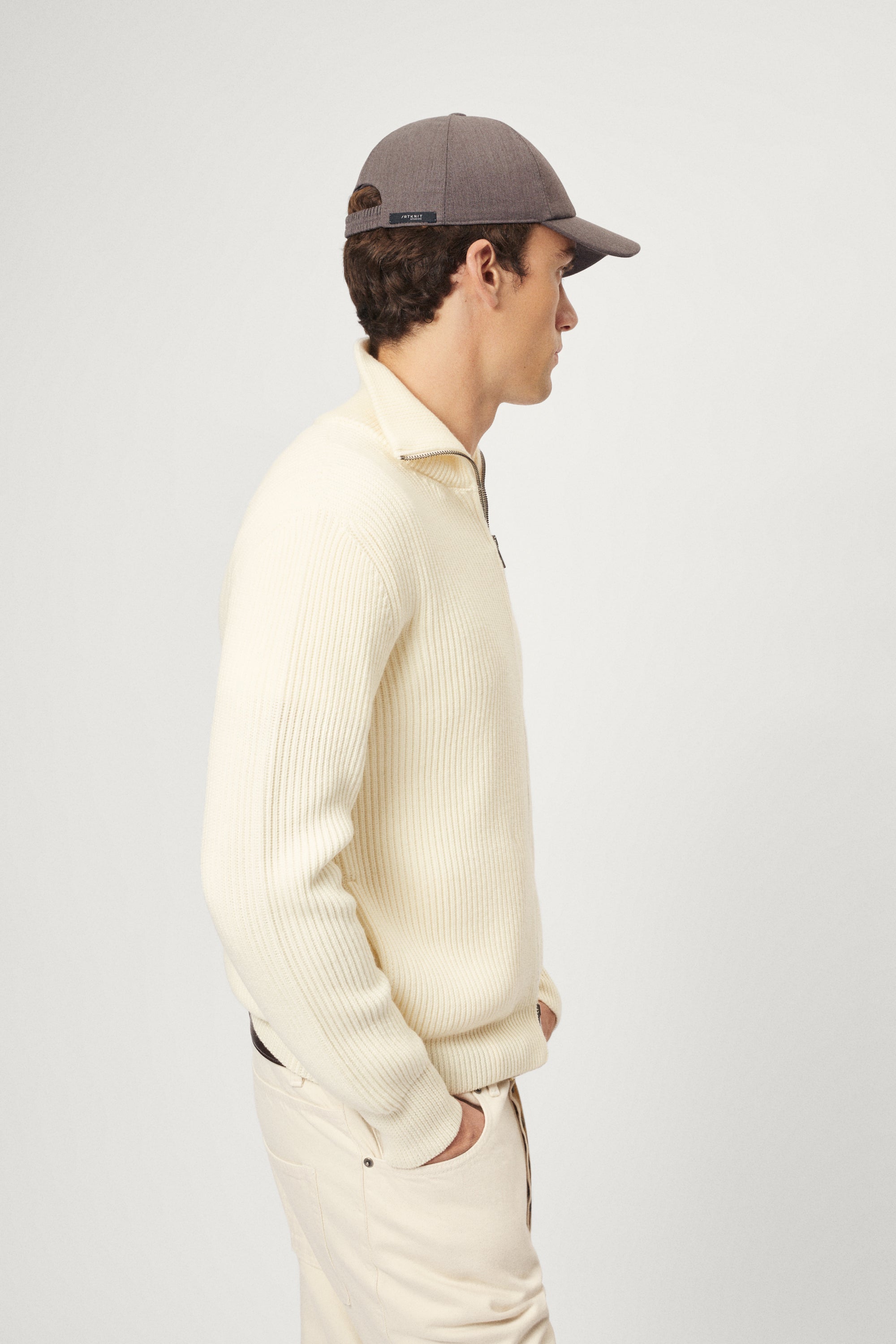 Person wearing a beige sweater and pants with a taupe hat on a white background