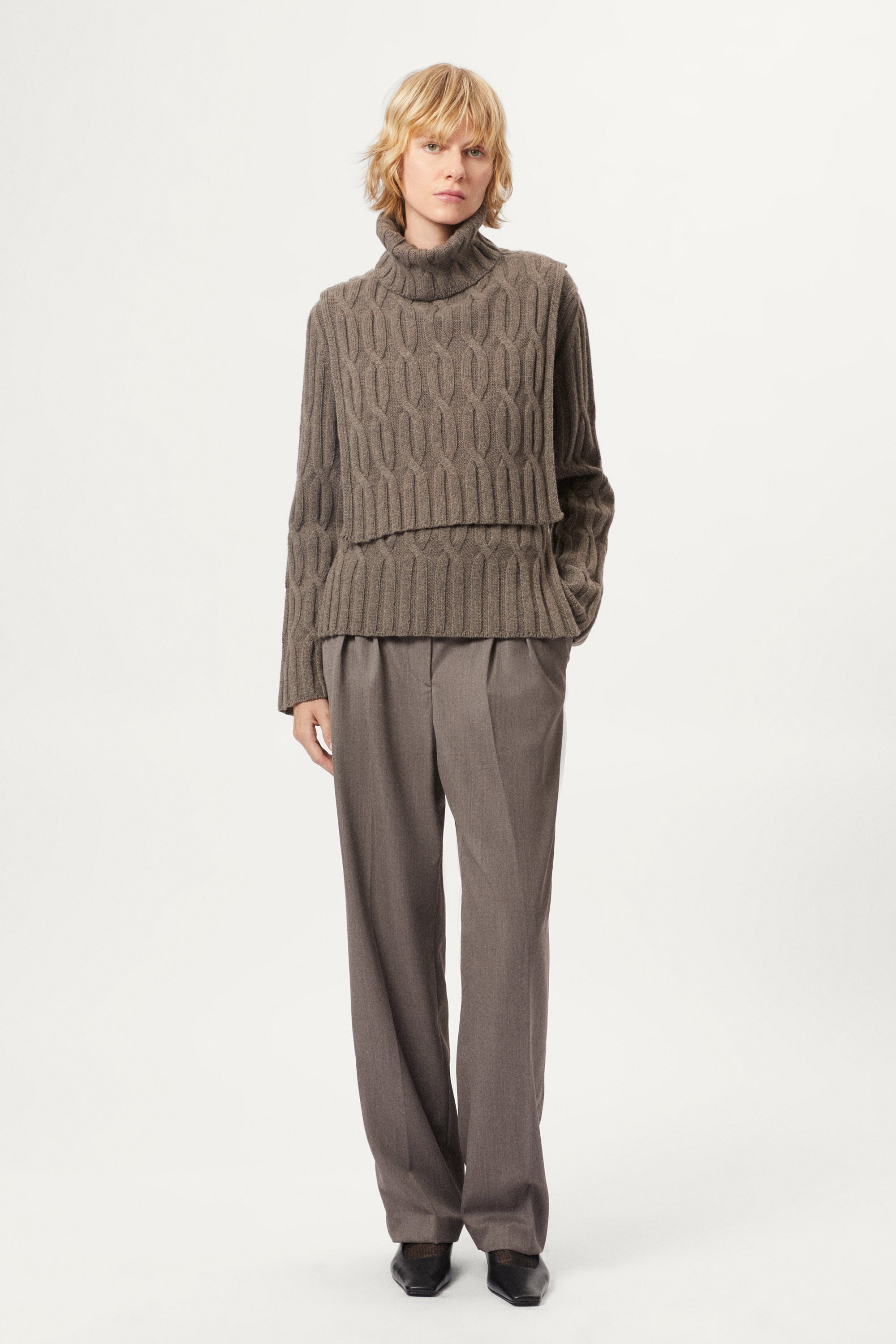 Woman wearing a brown cable knit bib and pants on a white background