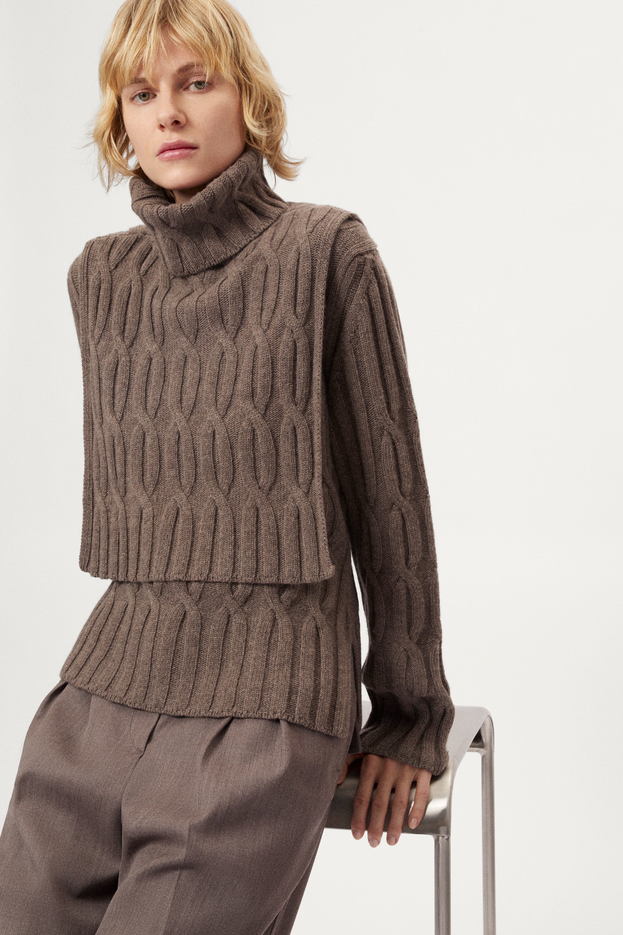 Woman wearing a brown cable knit bib and pants on a white background