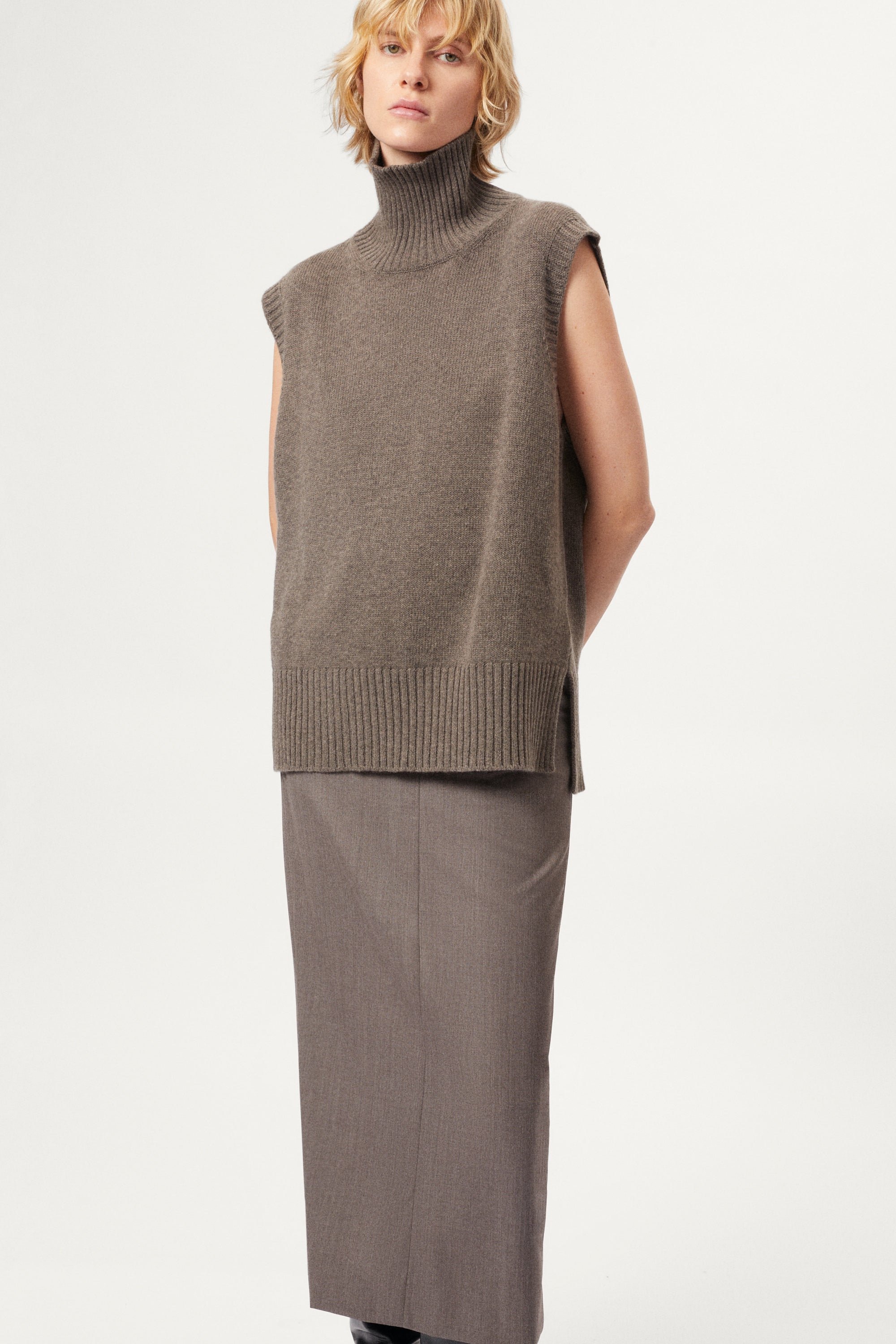 woman wearing a wool brown sleeveless high neck knitted top and skirt set on a white background