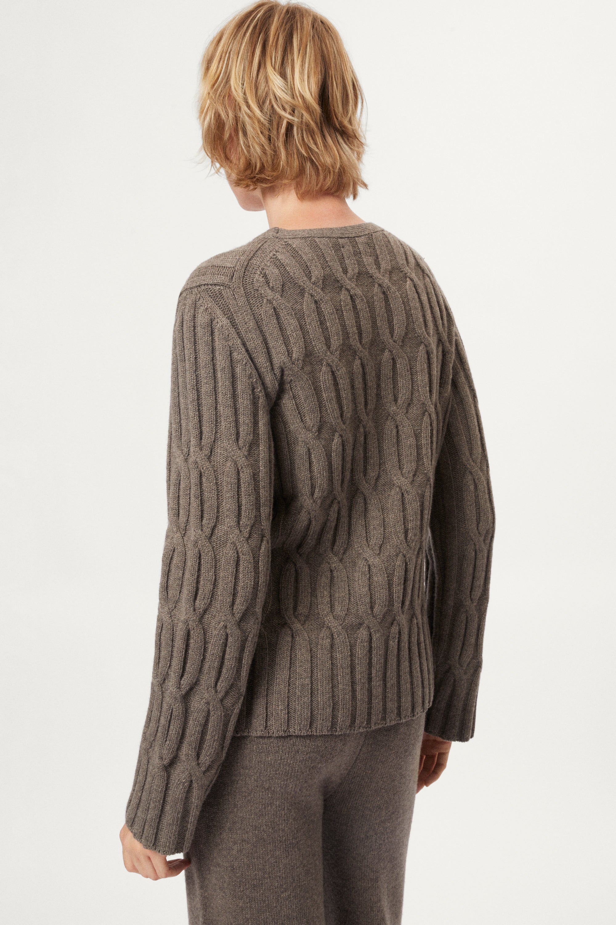Woman wearing a woolen taupe cable knit sweater and pants on a white background