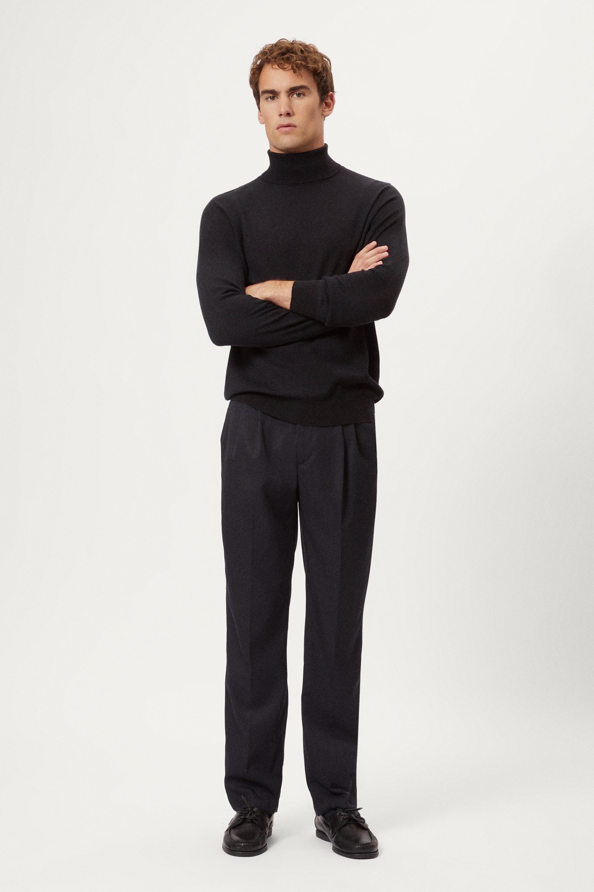 Man wearing a dark blue turtleneck sweater and pants on a white background