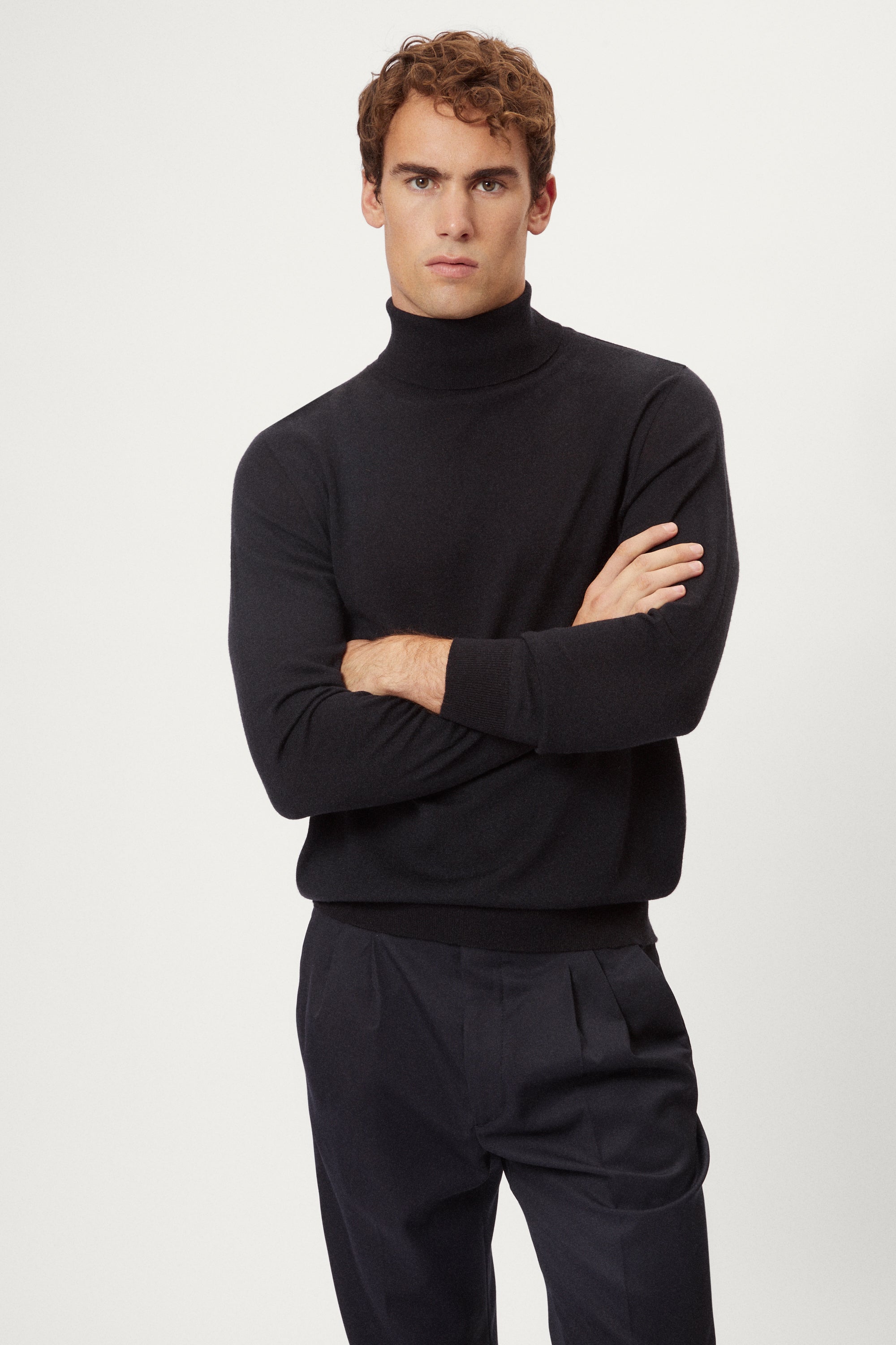 Man wearing a dark blue turtleneck sweater and pants on a white background