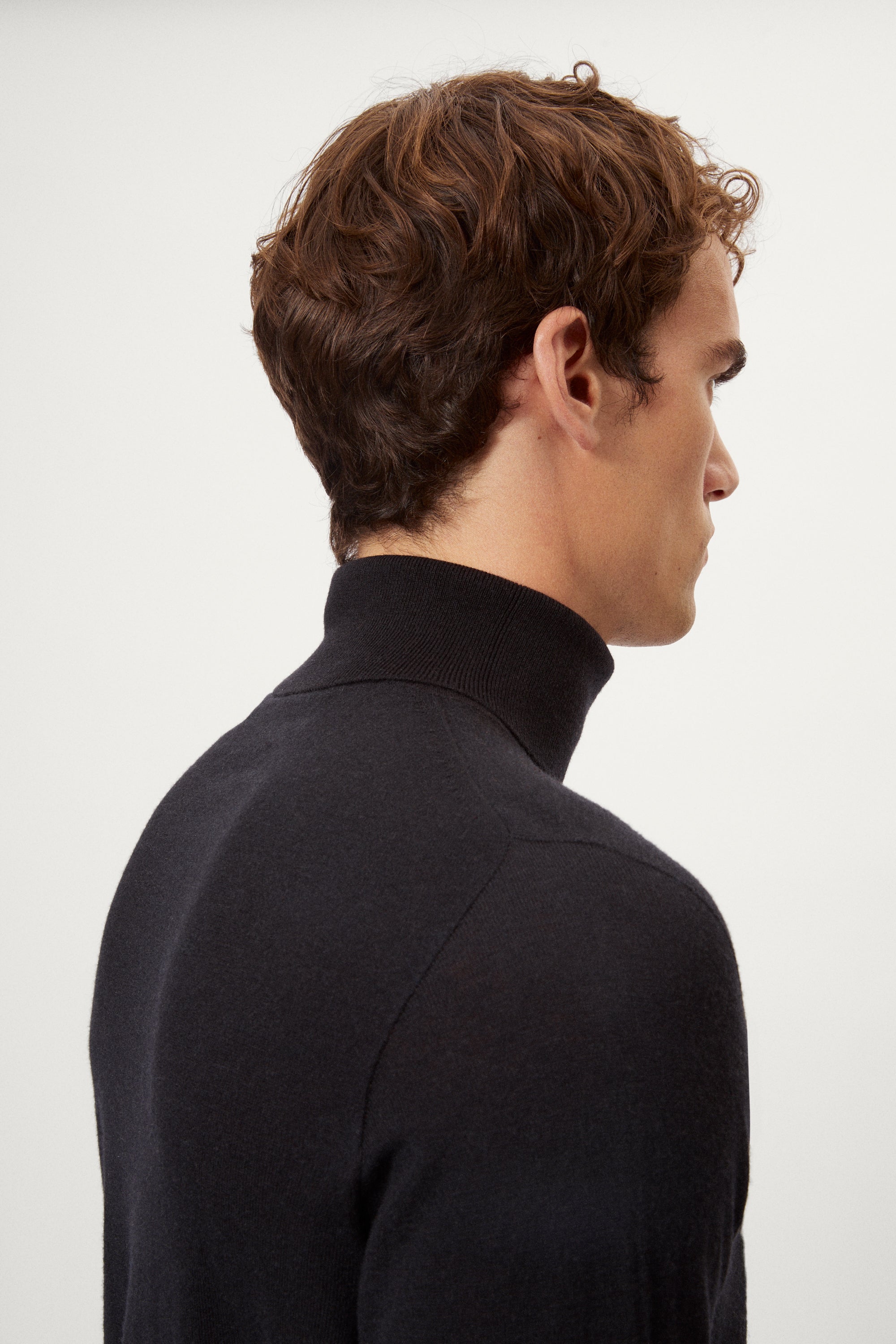 Man wearing a dark blue turtleneck merino sweater and pants on a white background