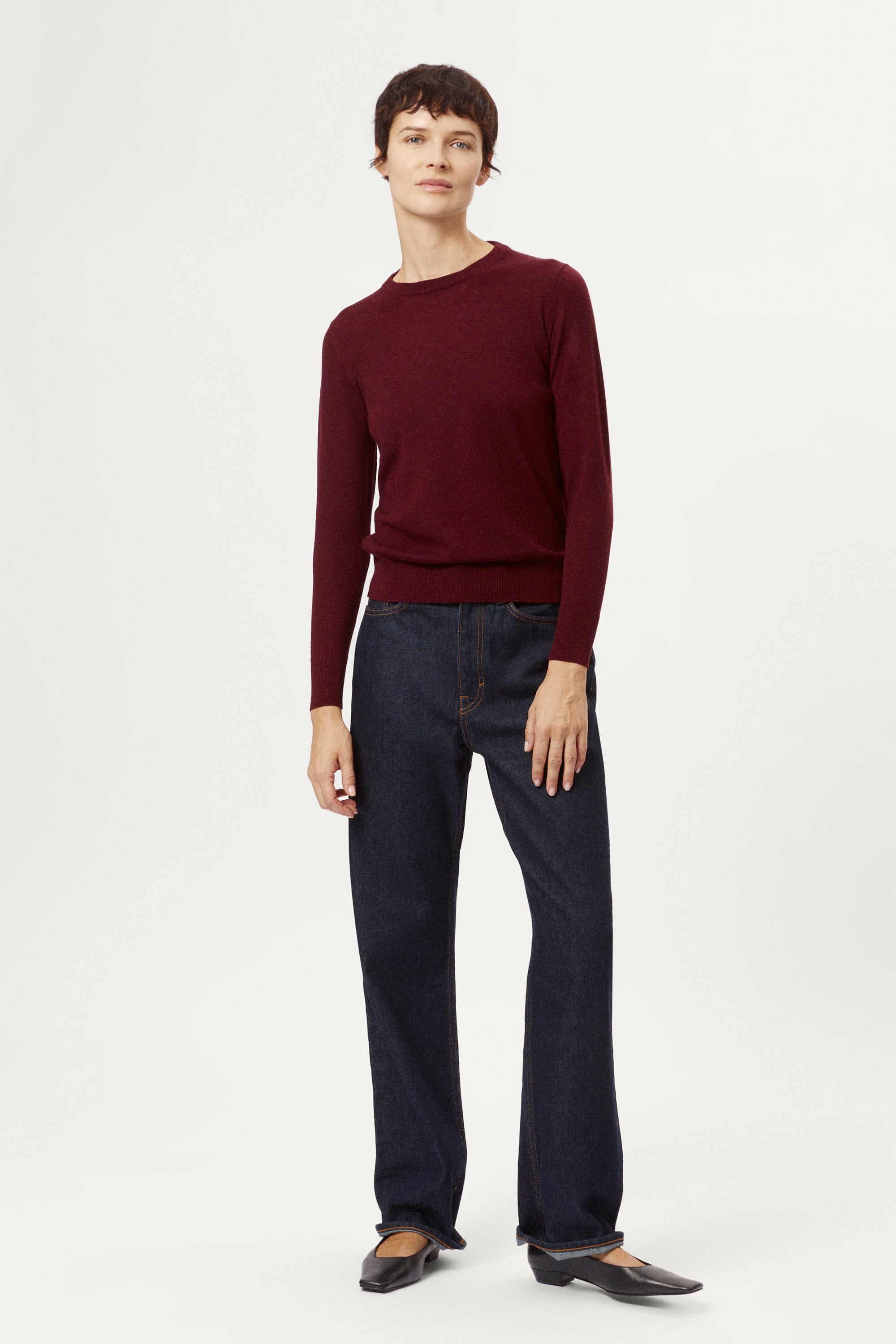 Person wearing a burgundy sweater and dark jeans on a white background