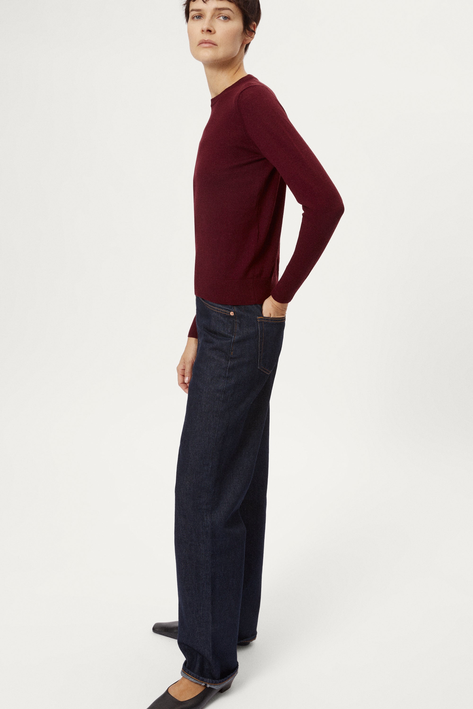 Person wearing a burgundy sweater and dark jeans on a white background