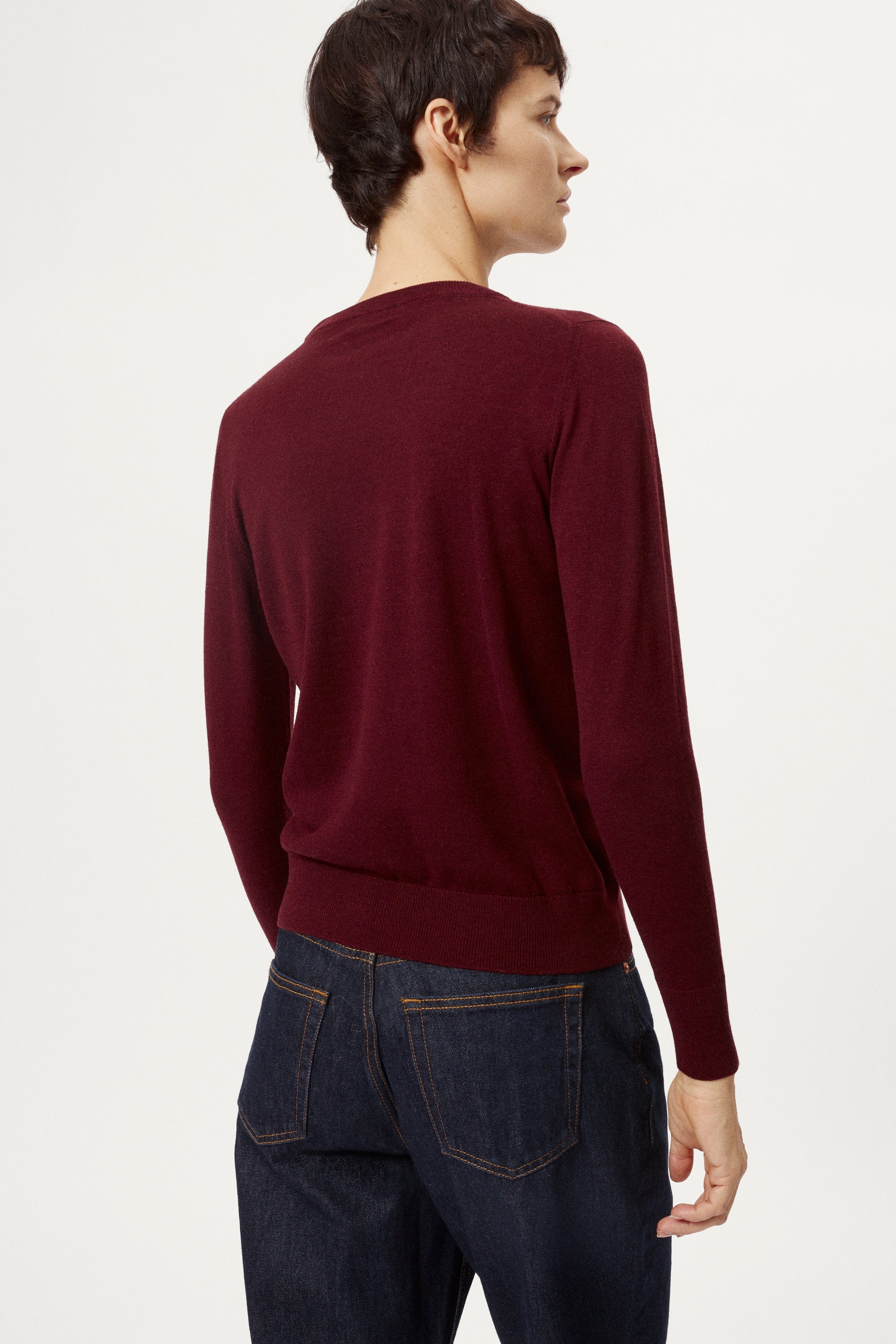 Person wearing a burgundy sweater and dark jeans on a white background