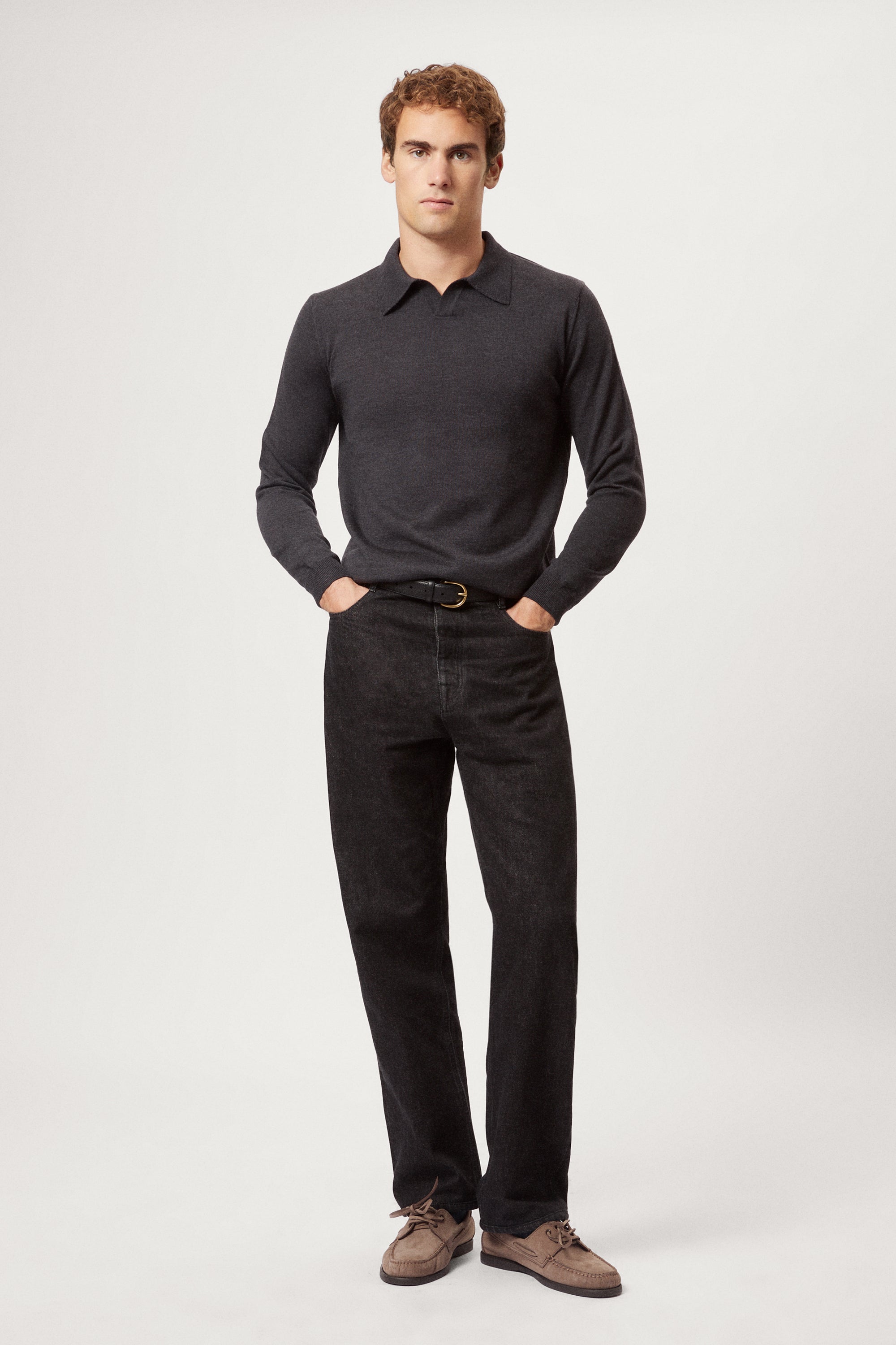 Man wearing a dark gray merino polo and black pants on a white background