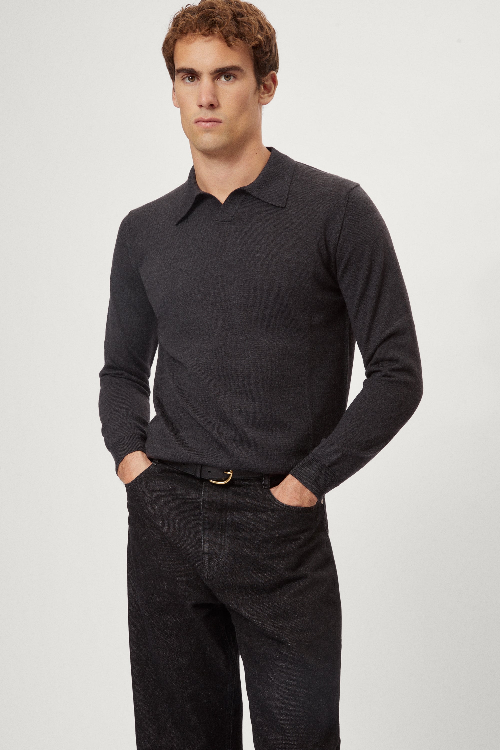 Man wearing a dark gray merino polo and black pants on a white background