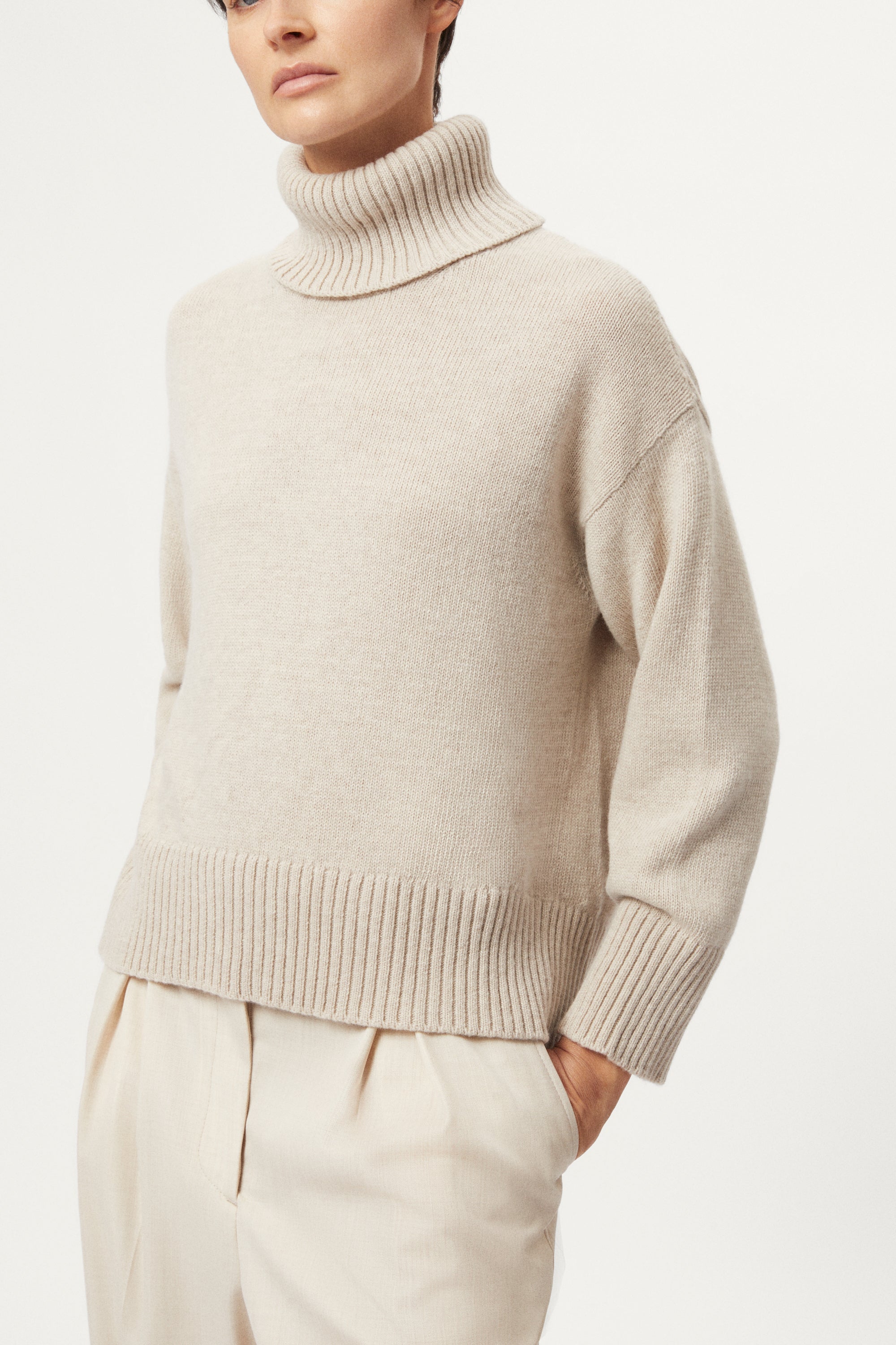 woman wearing a woolen beige sweater and wool pants on a white background