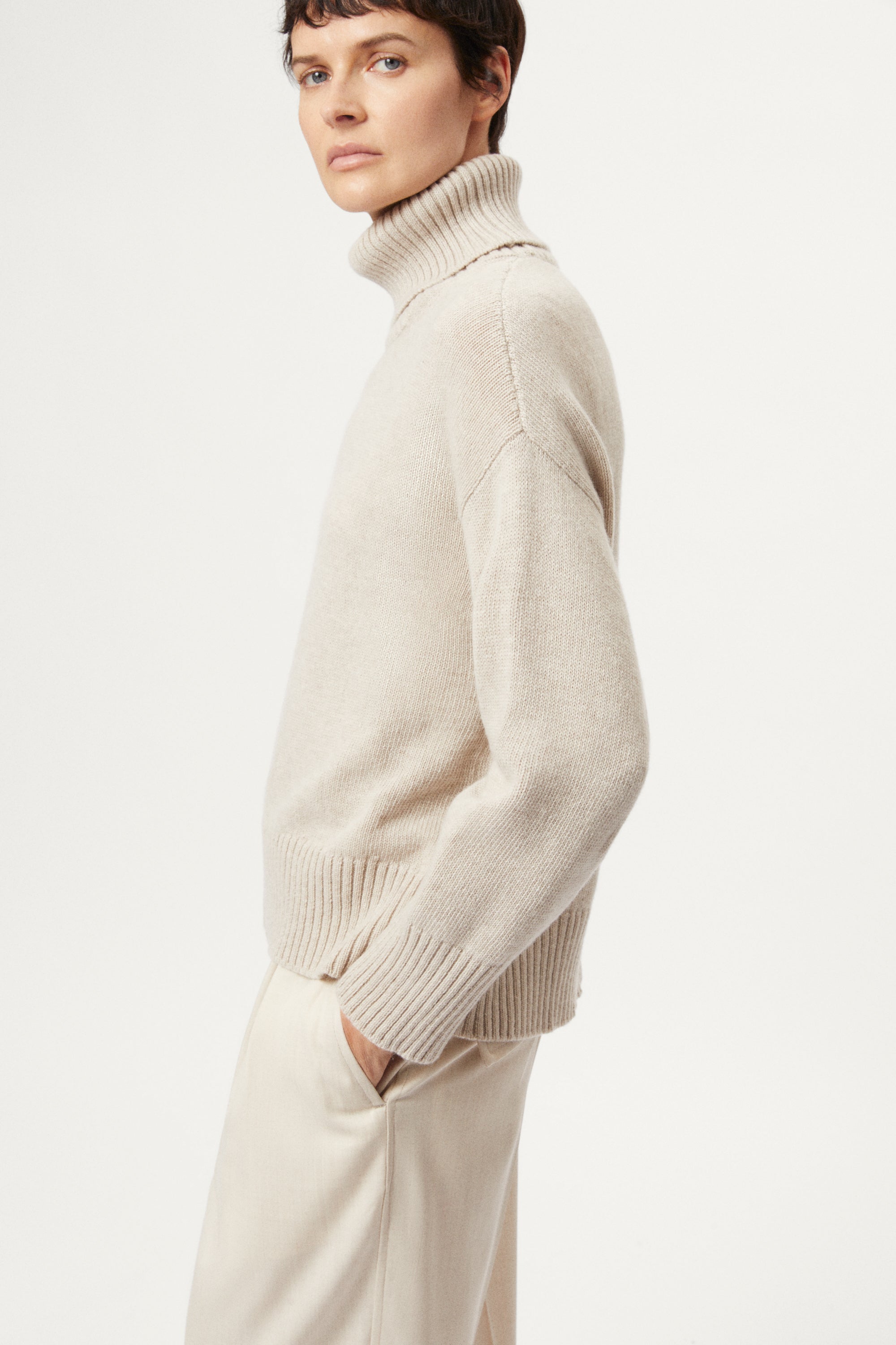 woman wearing a woolen beige sweater and wool pants on a white background