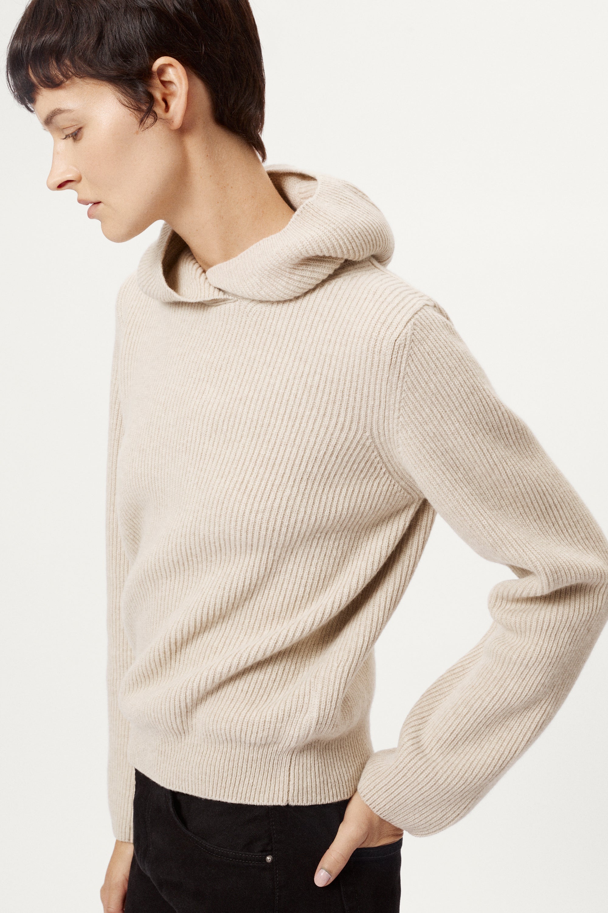 Person wearing a woolen ecru hoodie sweater on a white background
