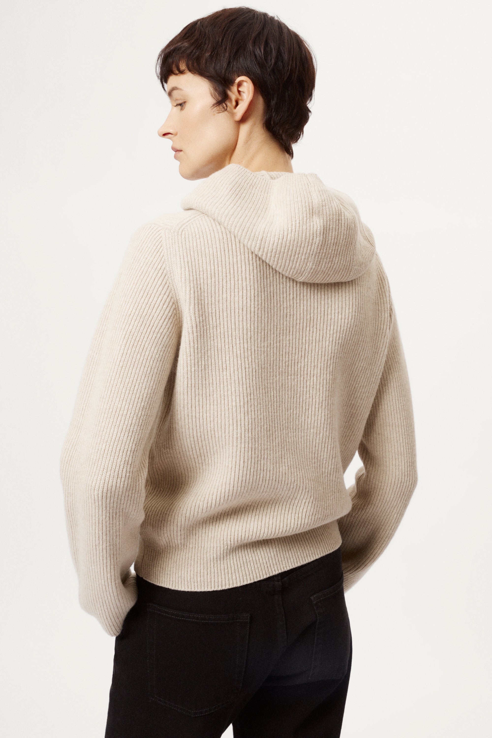 Person wearing a woolen ecru hoodie sweater on a white background