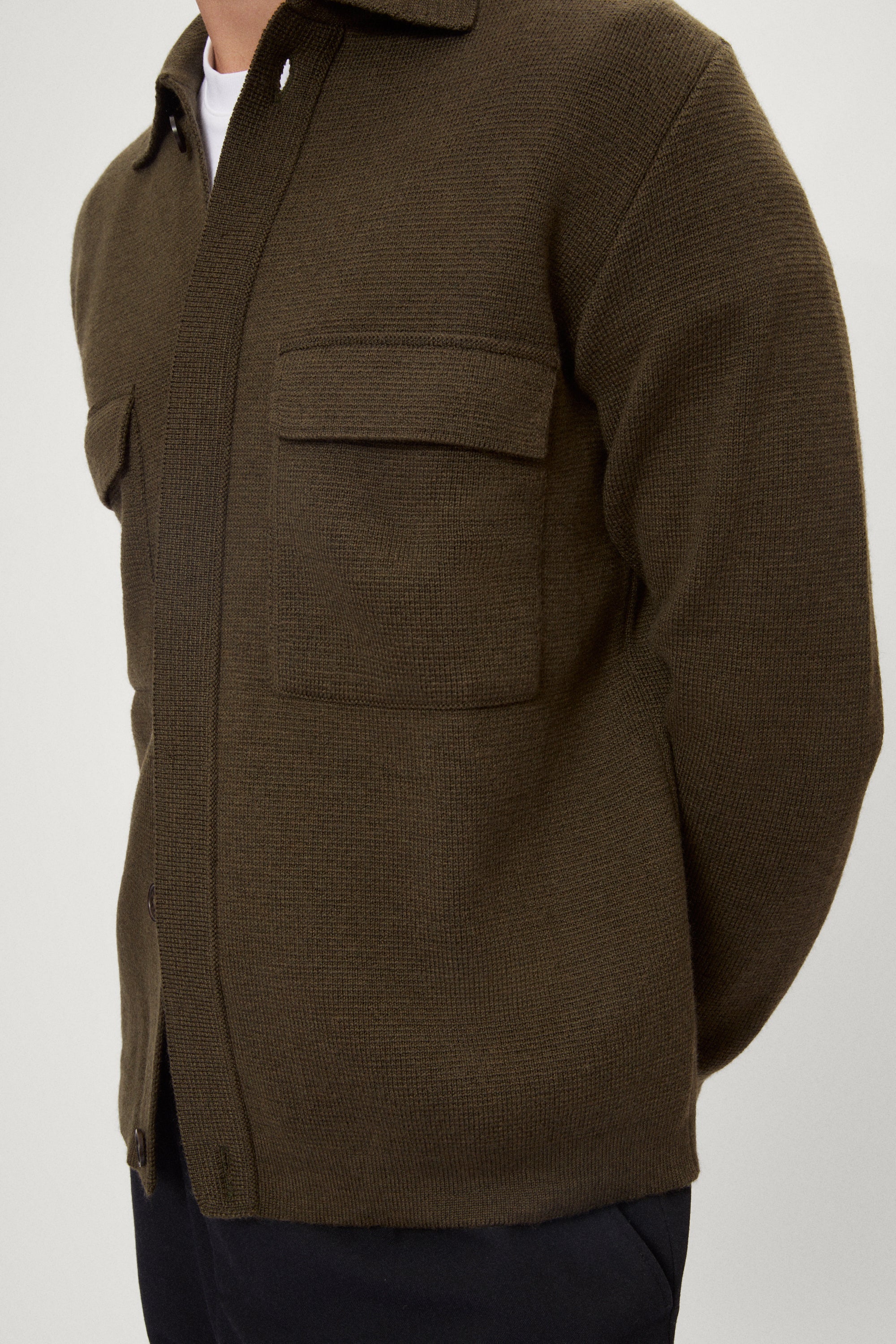 Man wearing a merino green jacket, white t-shirt and blue pants on a white background