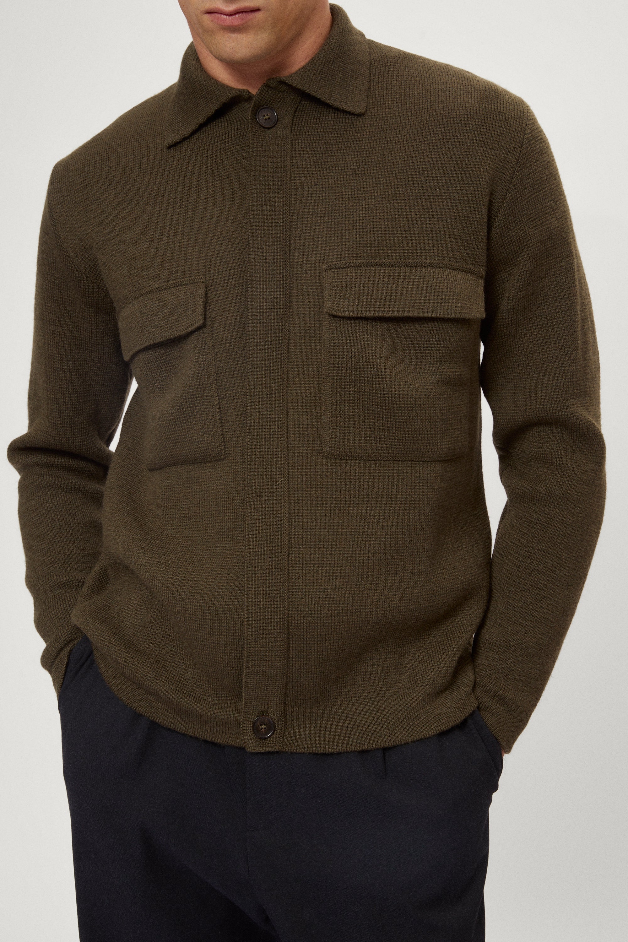 Man wearing a merino green jacket, white t-shirt and blue pants on a white background