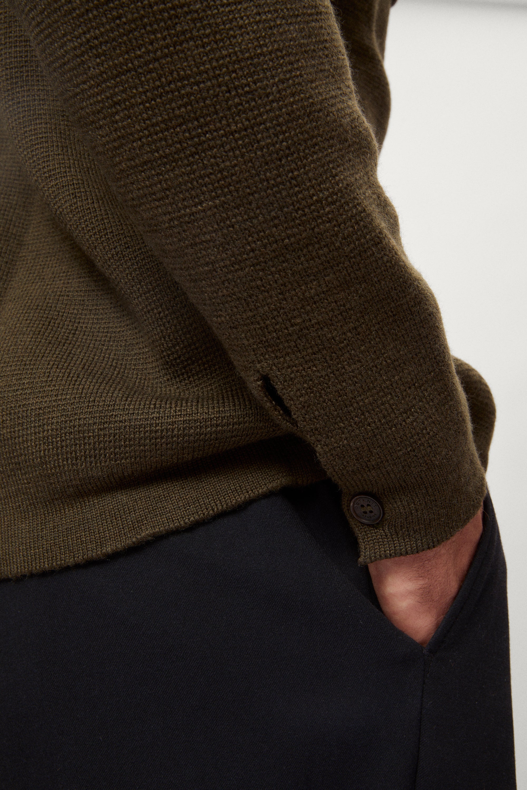 Close-up of Man wearing a merino green jacket, white t-shirt and blue pants on a white background