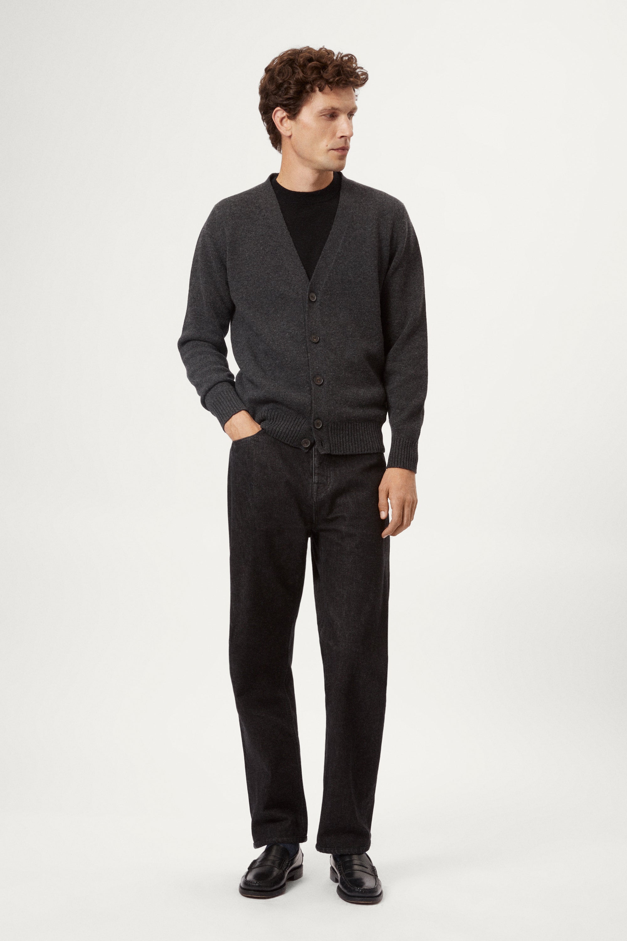 Man wearing a dark gray woolen cardigan over a black shirt on a white background