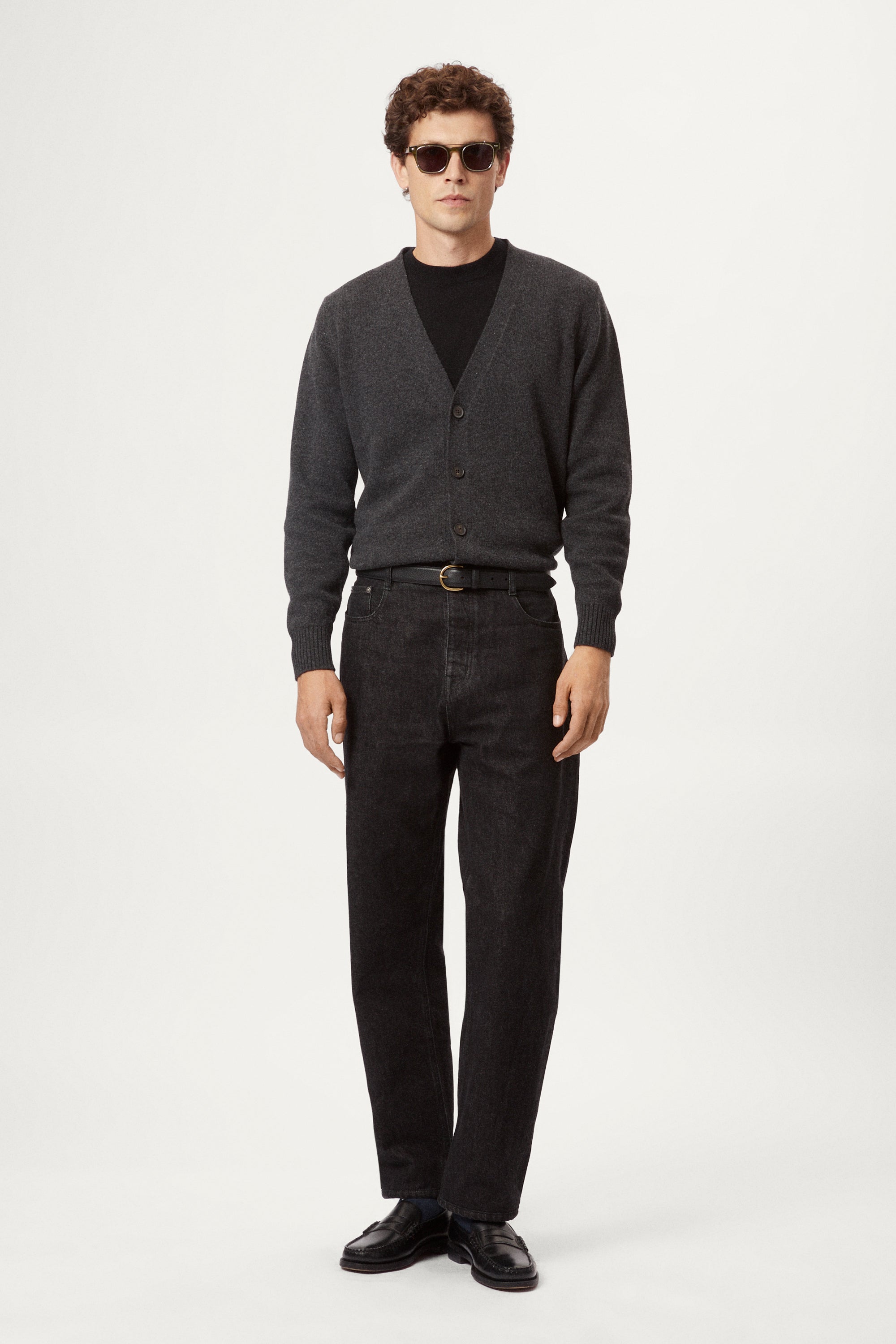 Man wearing a dark gray woolen cardigan over a black shirt on a white background