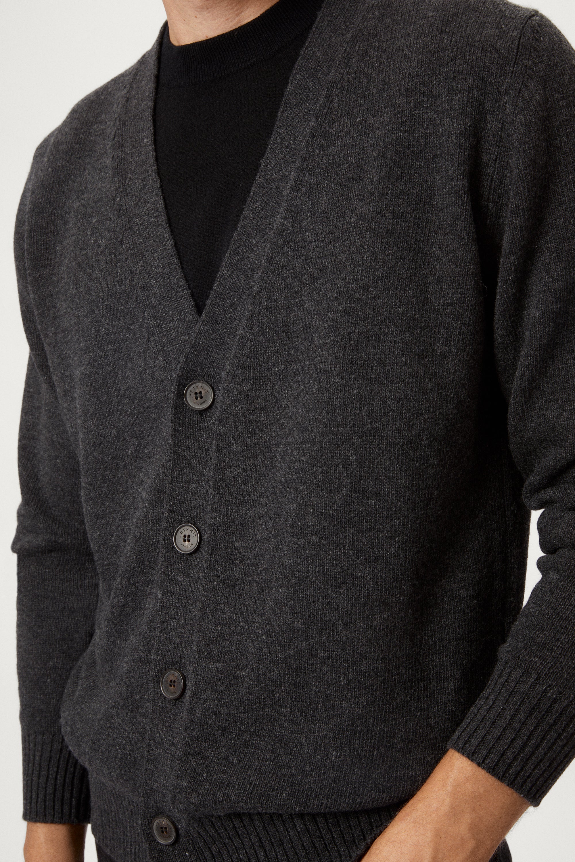 Man wearing a dark gray woolen cardigan over a black shirt on a white background