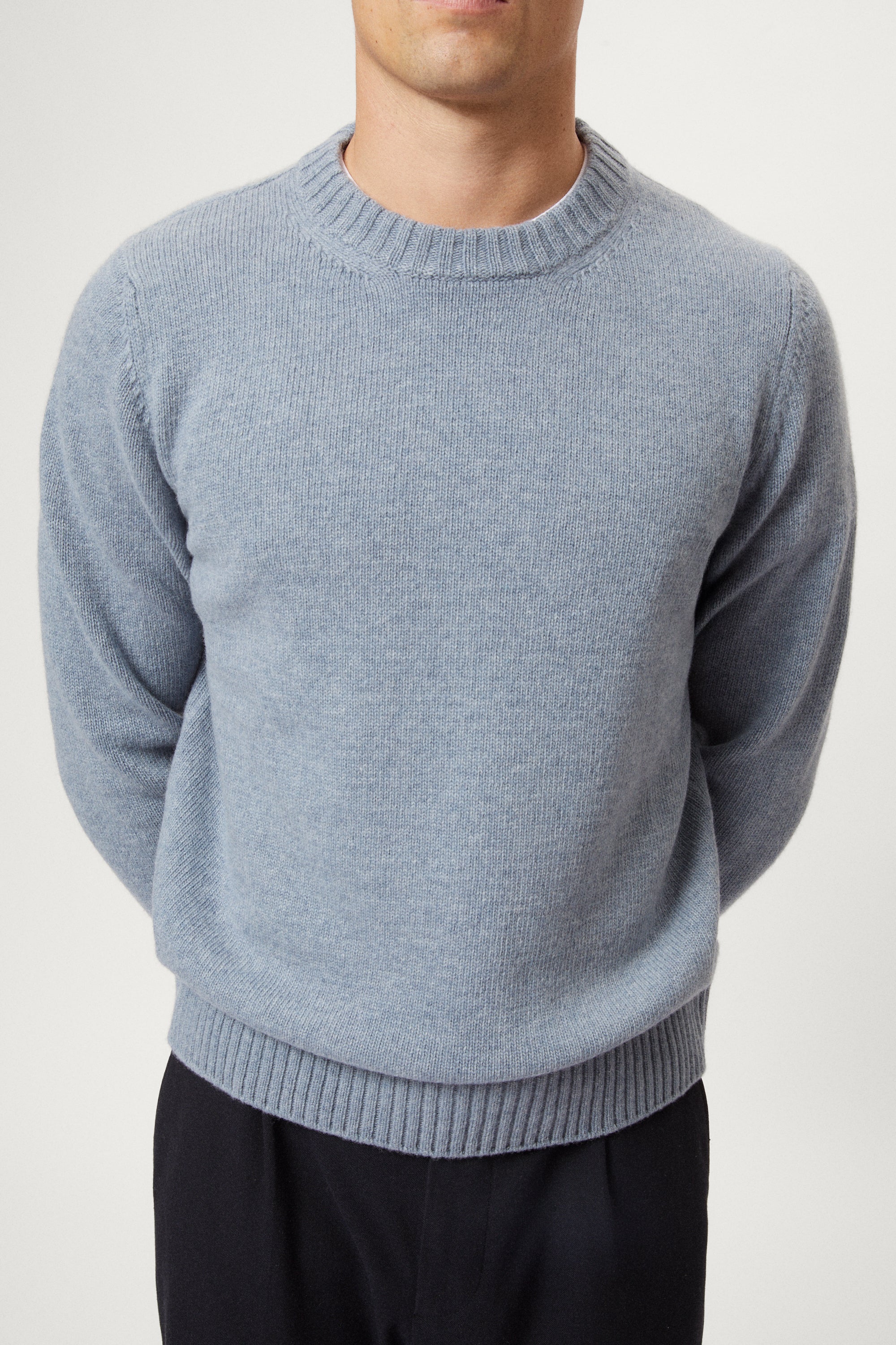 Man wearing a light blue woolen sweater and dark pants on a white background