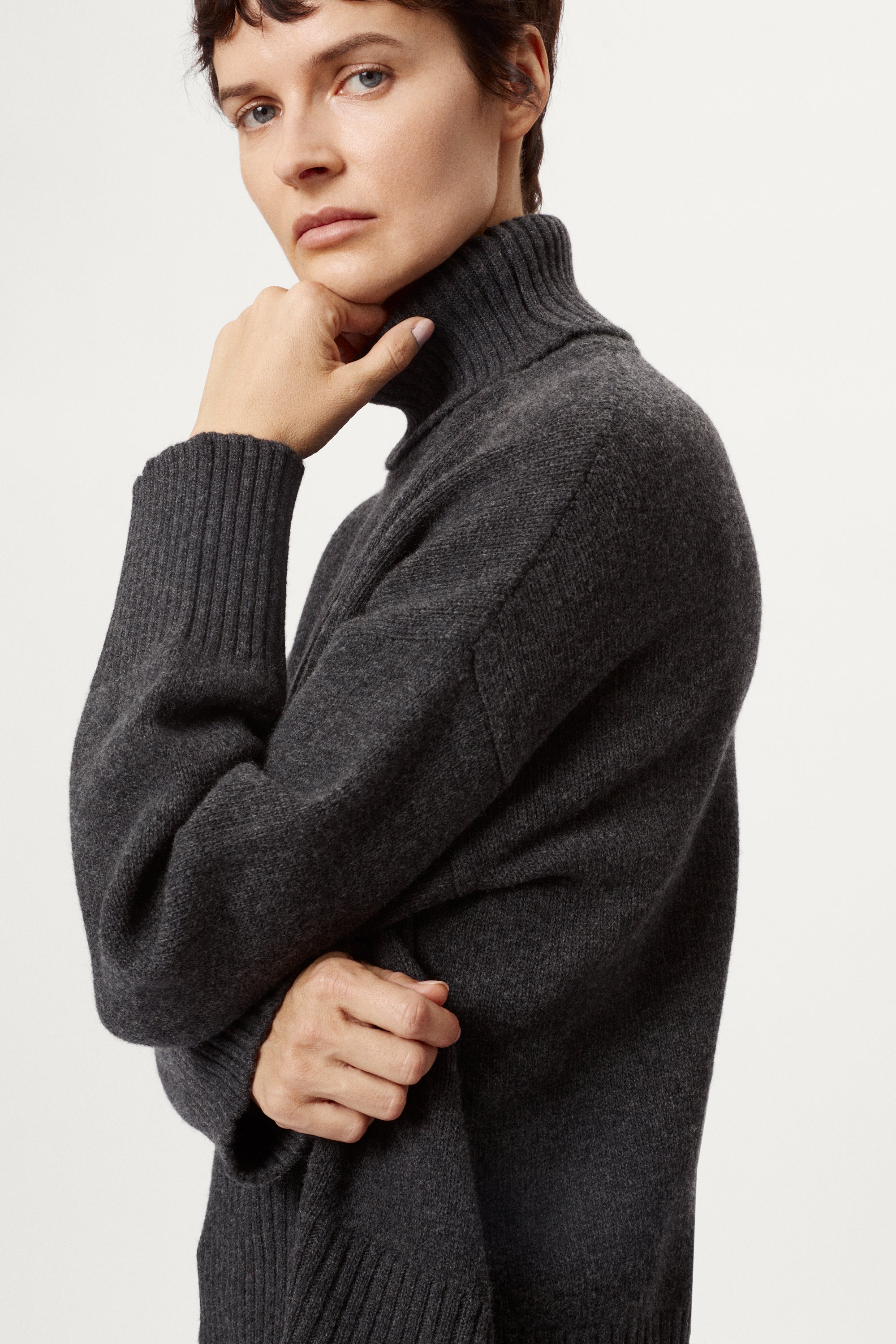 woman wearing a woolen dark grey turtleneck sweater and blue jeans on a white background