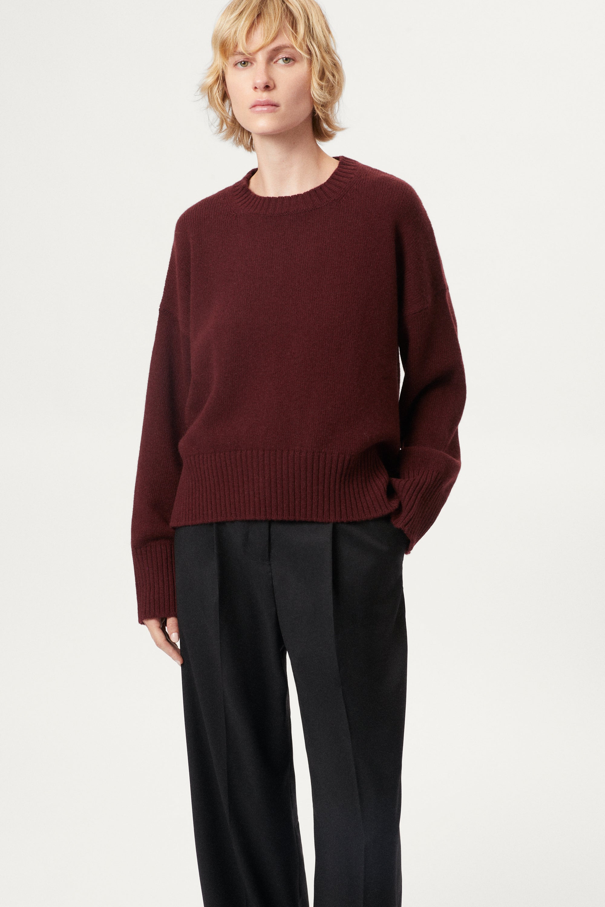 Woman wearing a woolen burgundy sweater and black pants on a white background