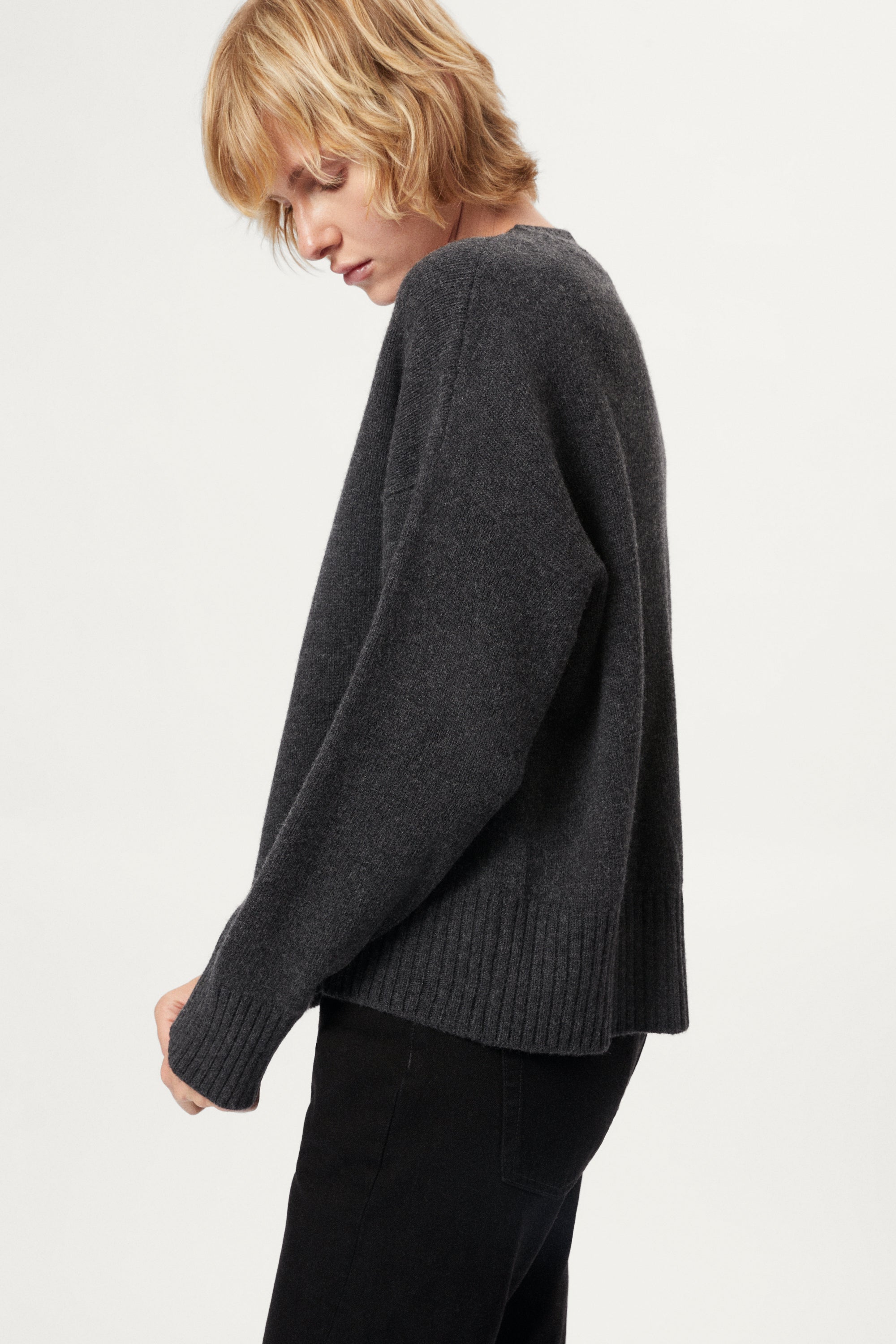 Woman wearing a woolen dark gray sweater and black pants on a white background