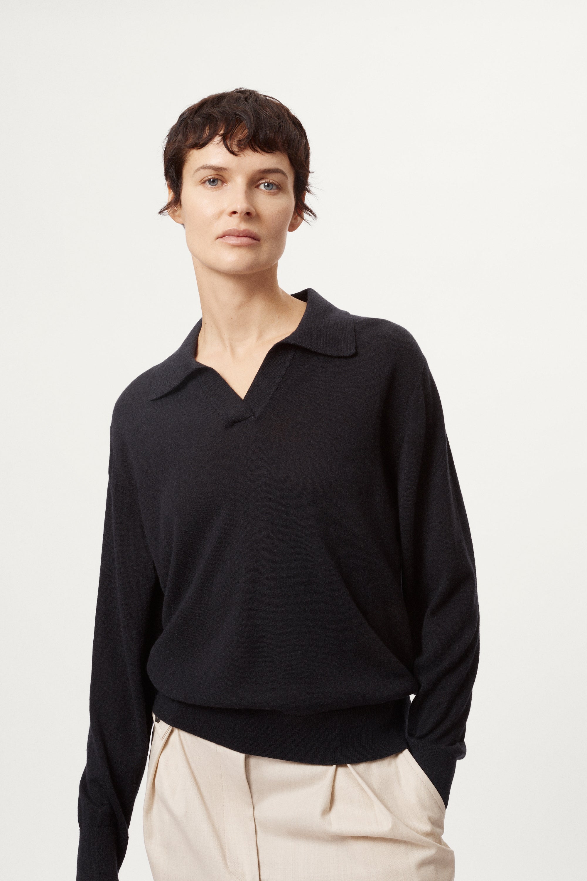 Person wearing a blue wool polo and beige pants on a white background