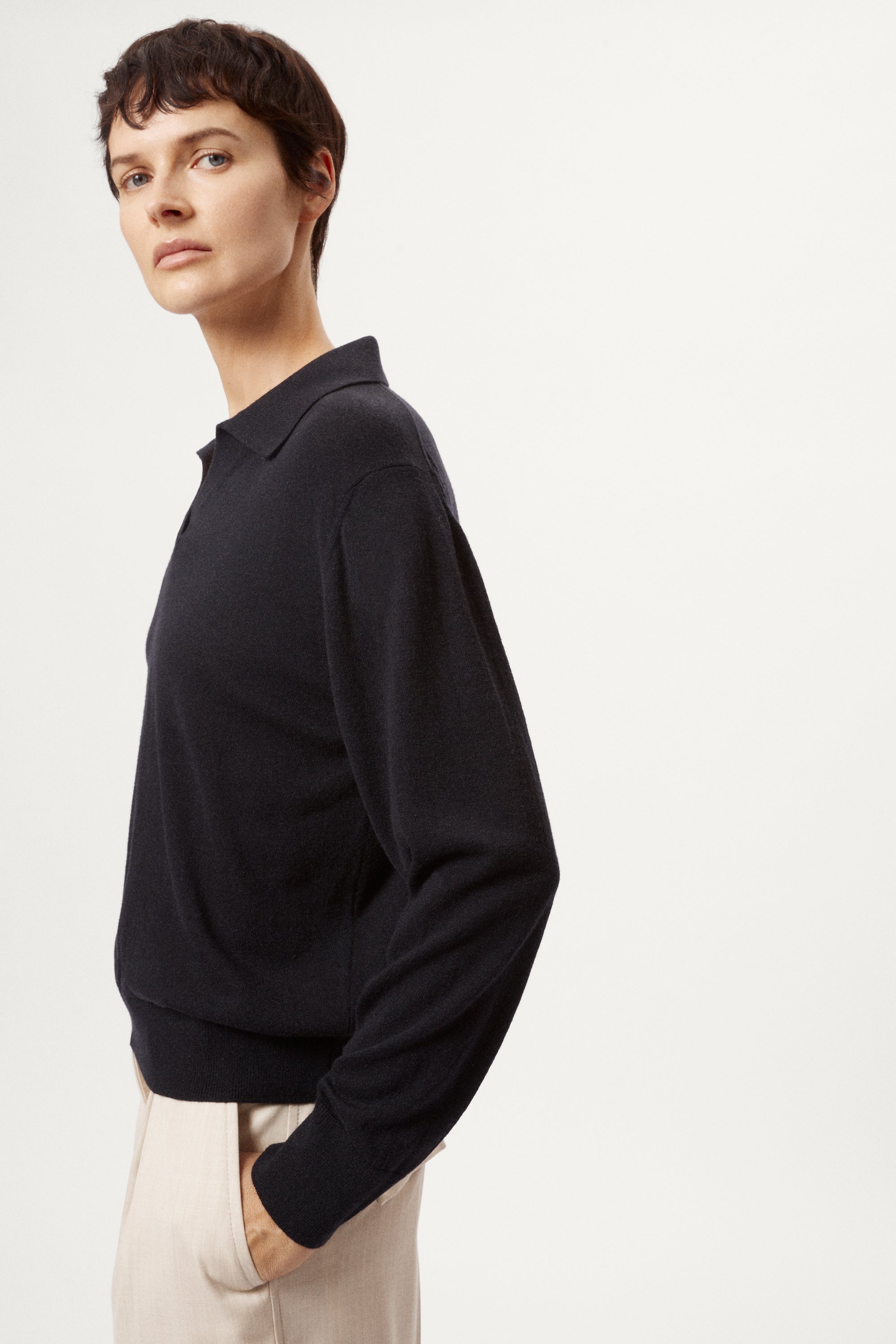 Person wearing a blue wool polo and beige pants on a white background