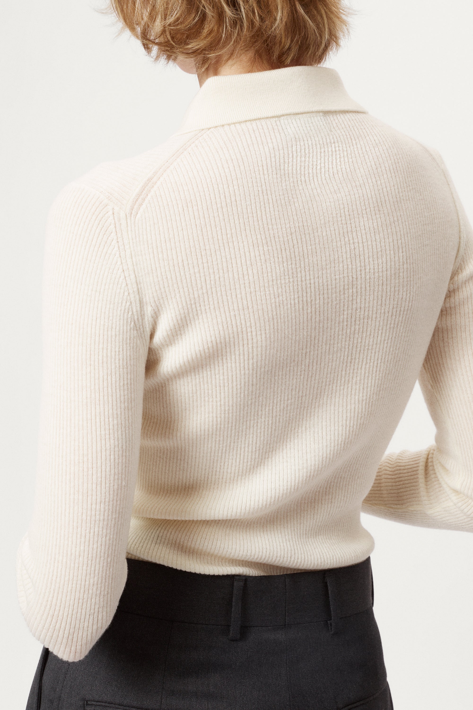 Woman wearing a white merino shirt and dark gray pants on a white background