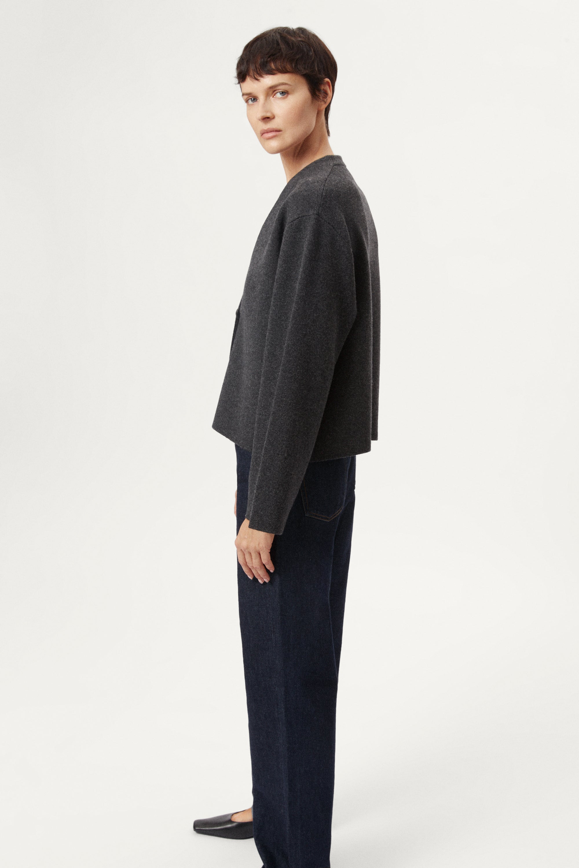 woman wearing a woolen dark gray cardigan with dark jeans on a white background