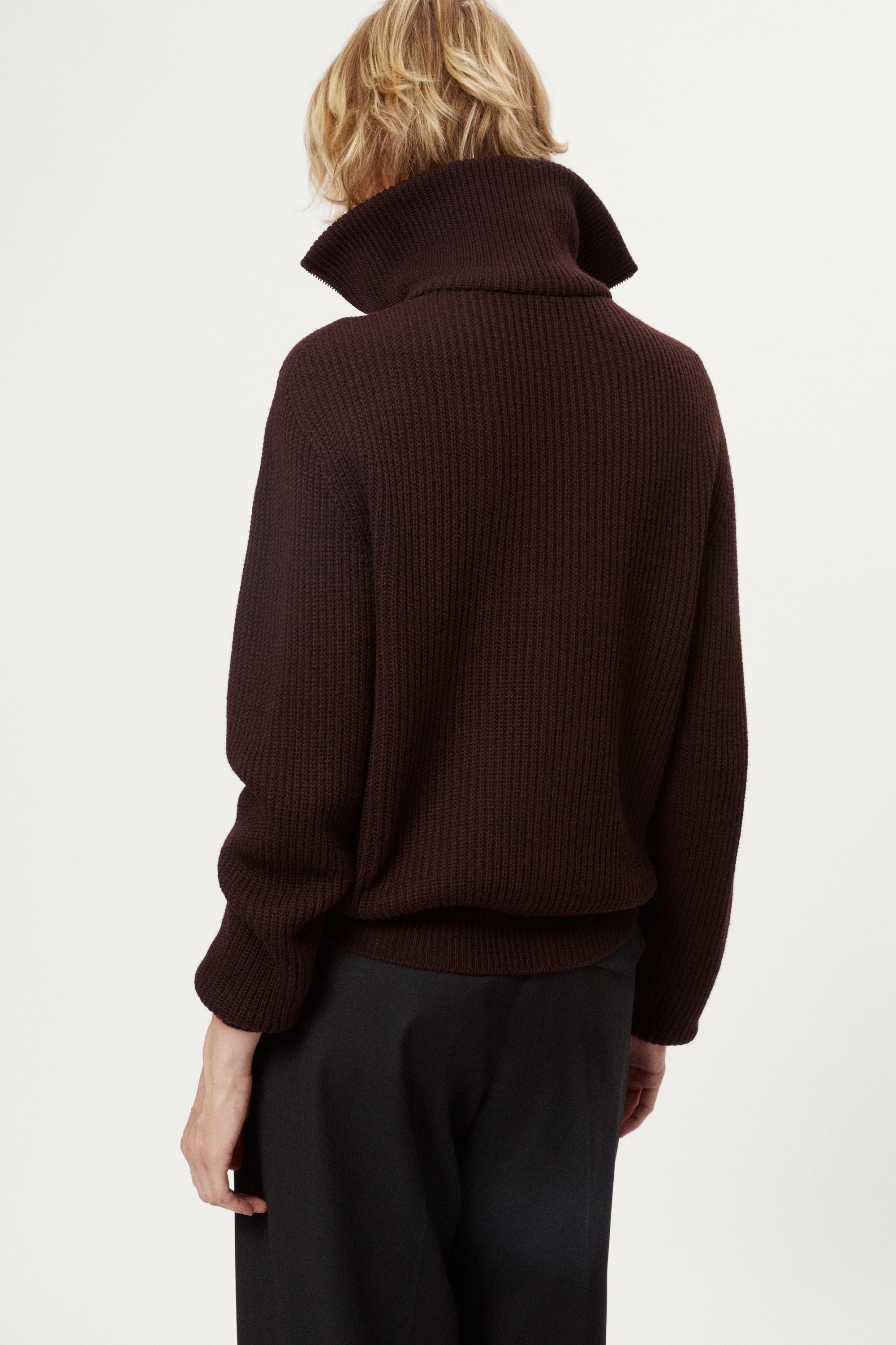 woman wearing a dark brown zip-up sweater and grey pants on a white background