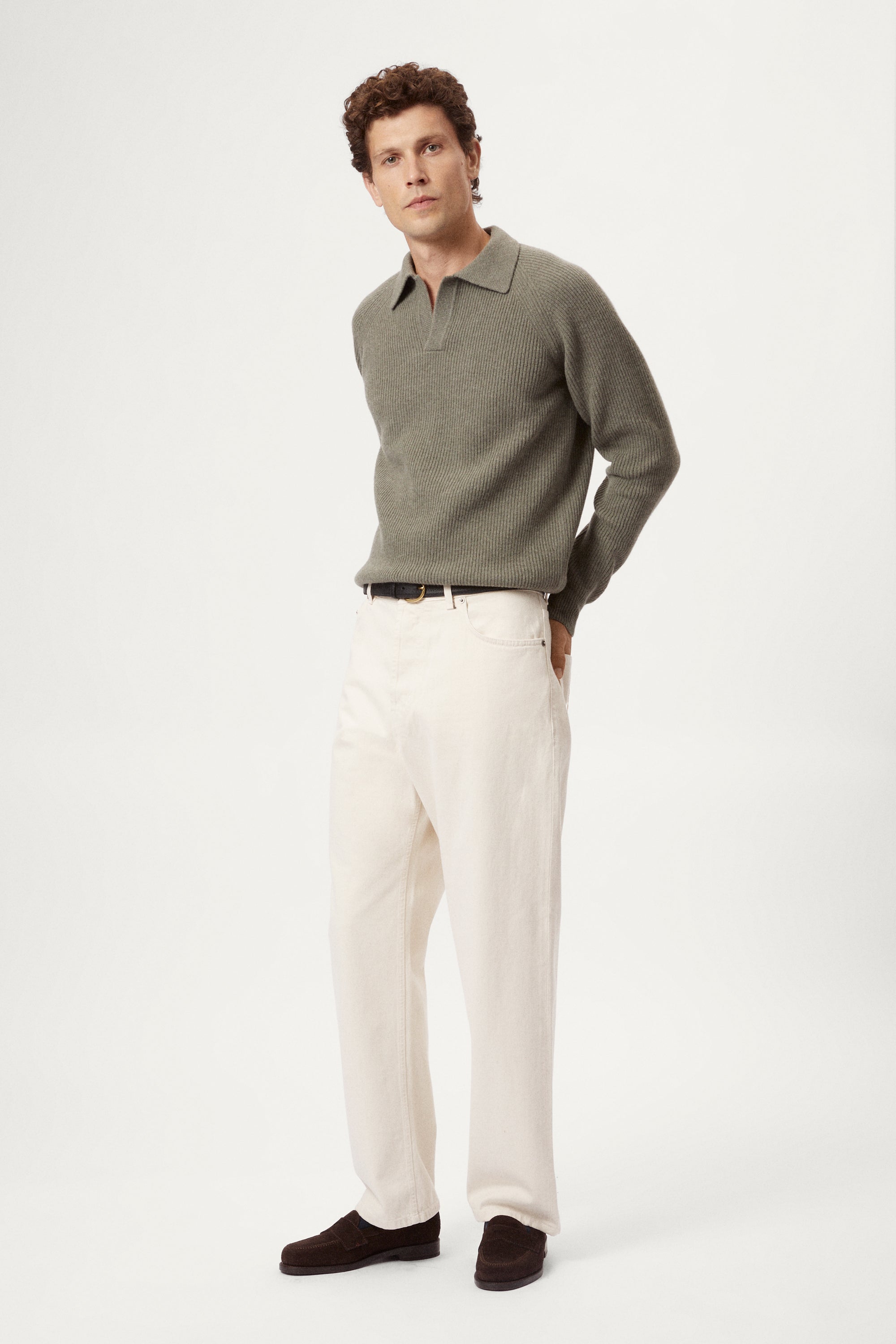 Man wearing a wool green polo sweater sweater and white pants on a white background