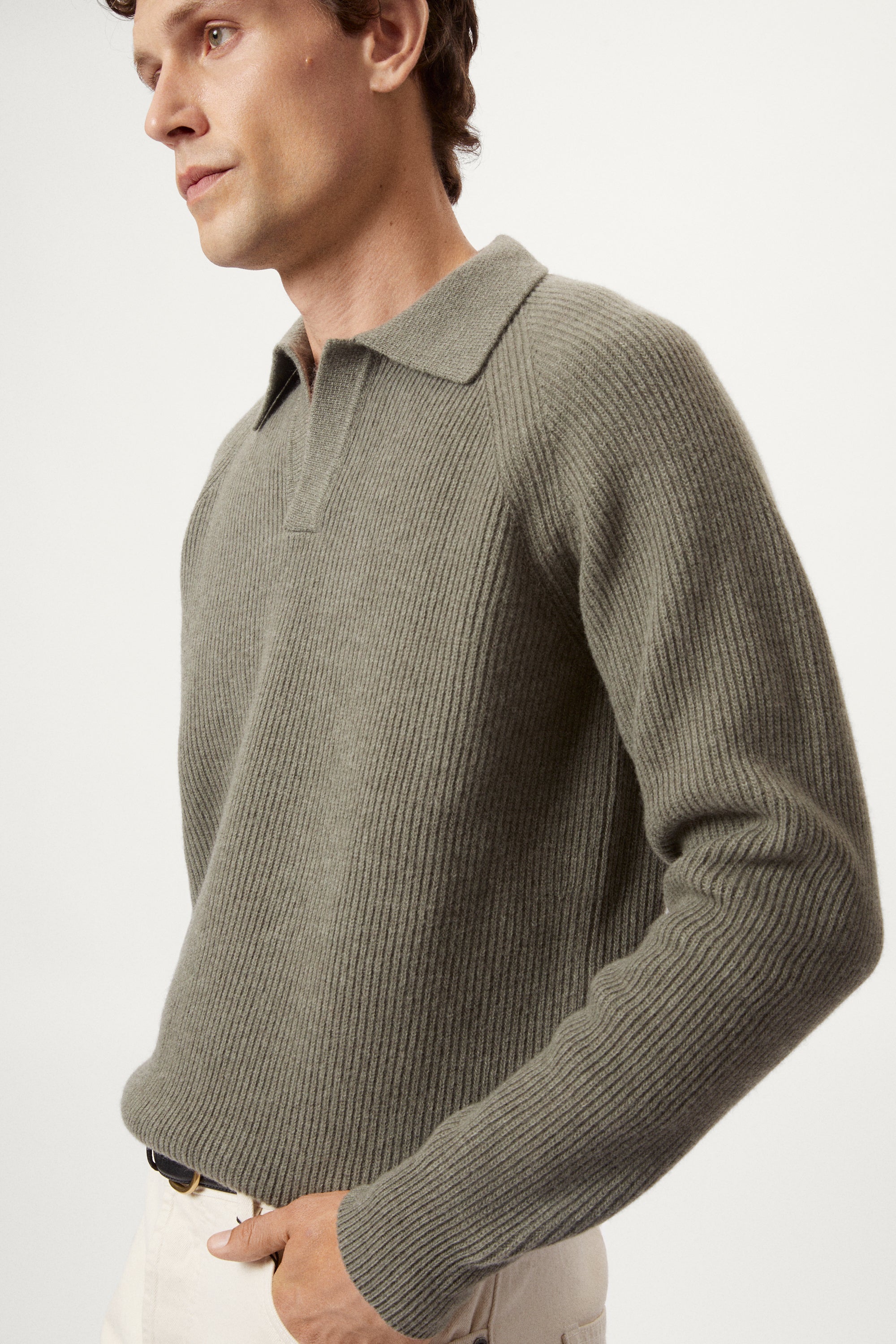 Man wearing a wool green polo sweater sweater and white pants on a white background
