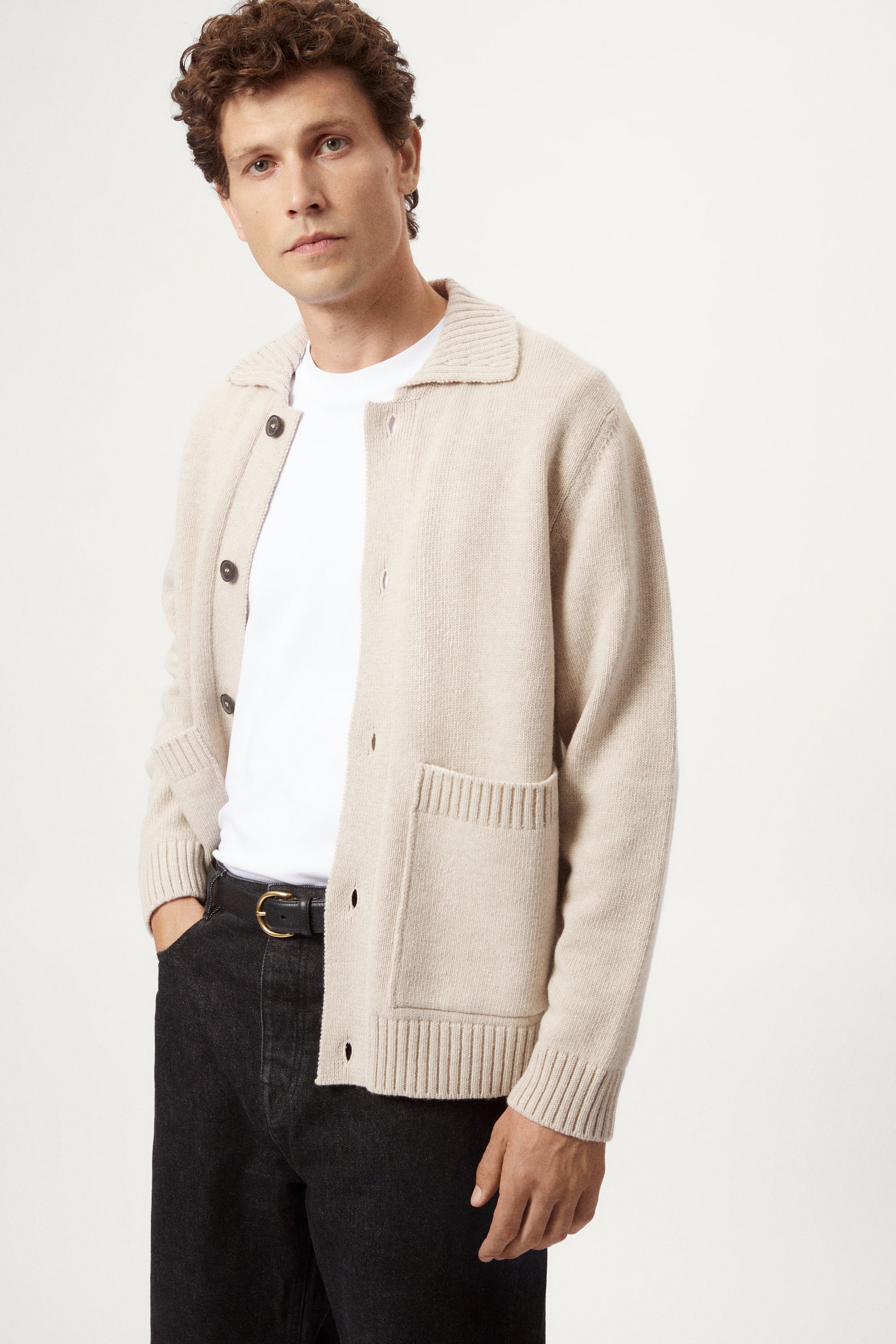 Man wearing a beige woolen jacket, black pants, and brown shoes on a white background