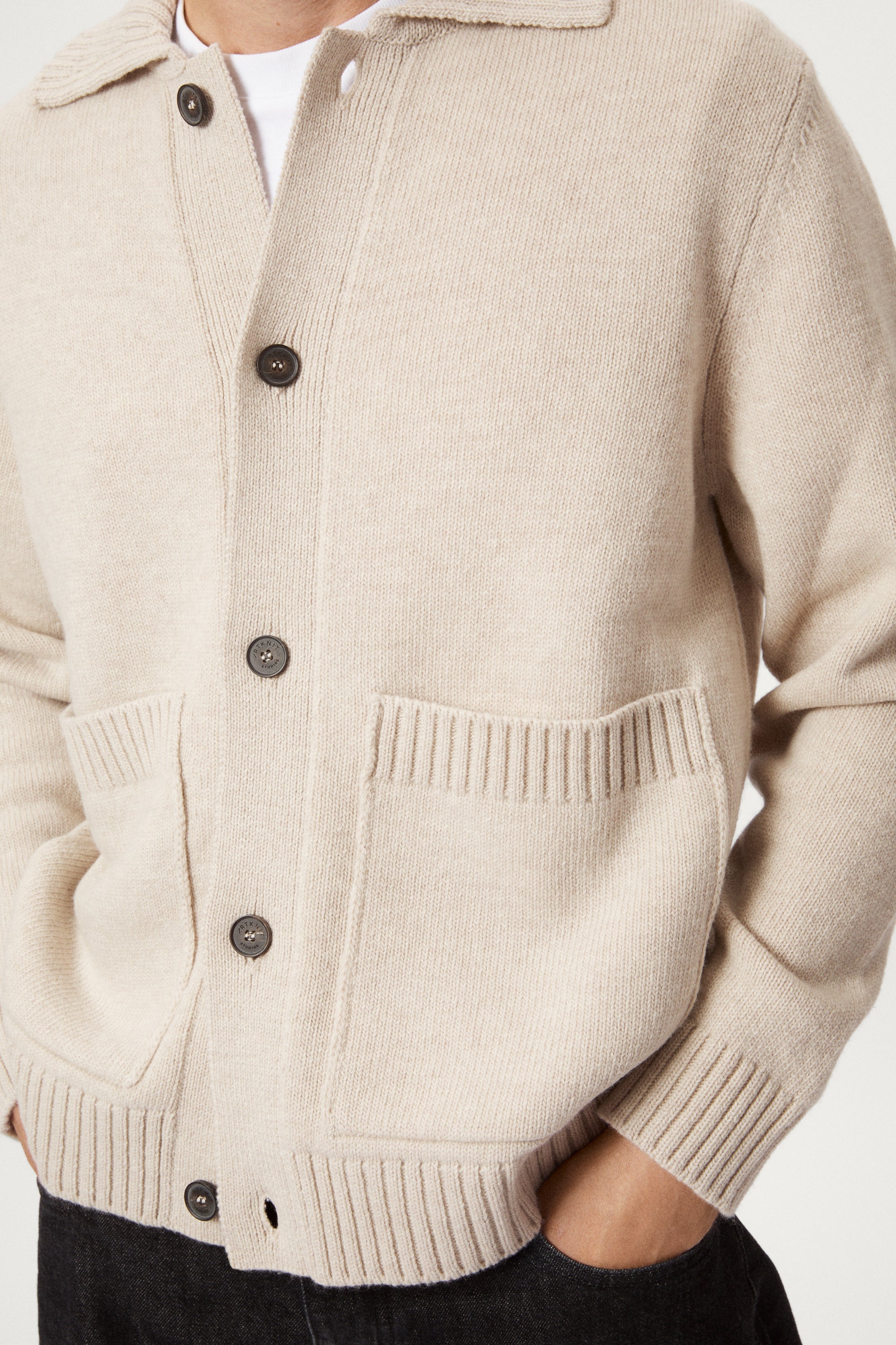 Man wearing a beige woolen jacket, black pants, and brown shoes on a white background