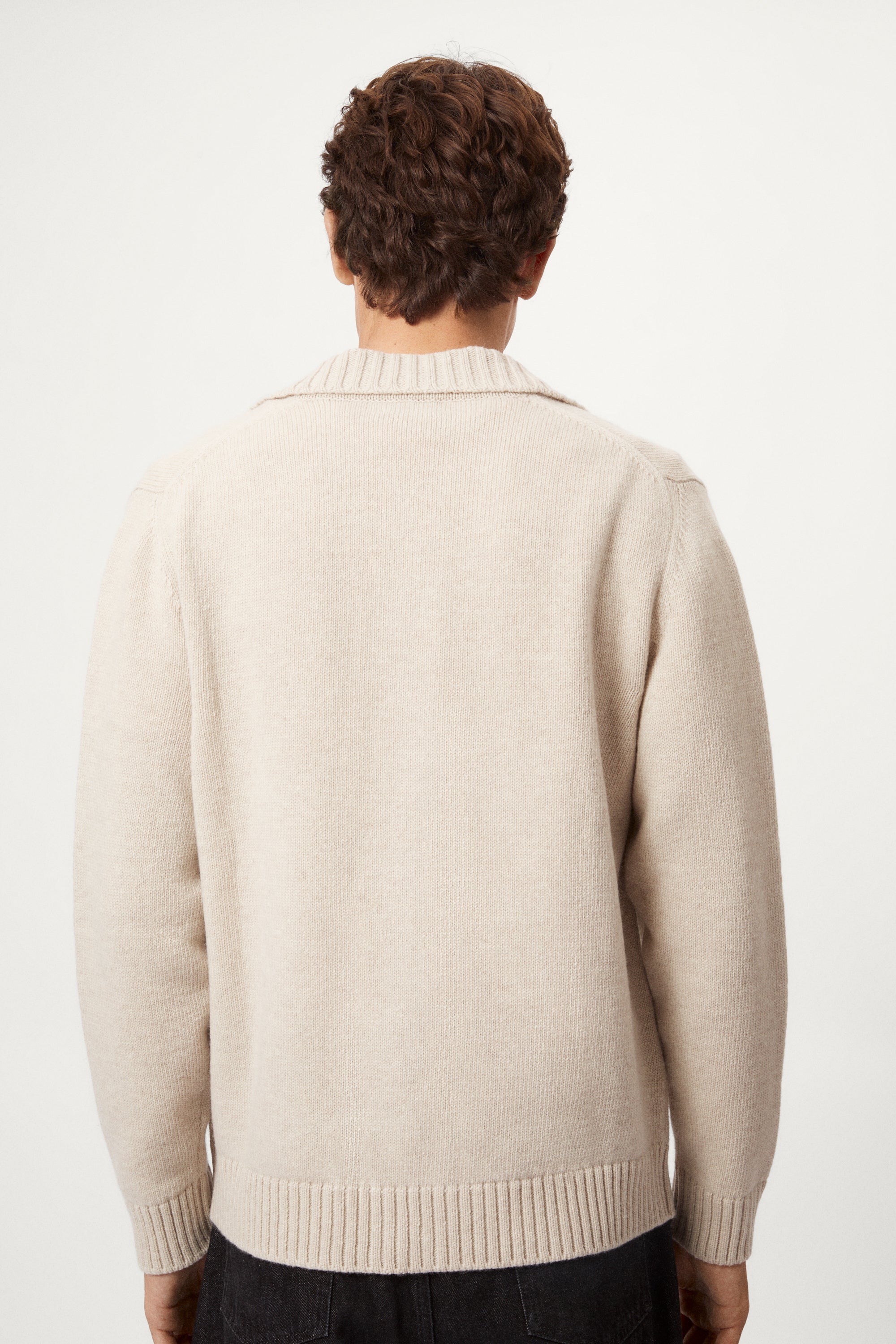 Man wearing a beige woolen jacket, black pants, and brown shoes on a white background