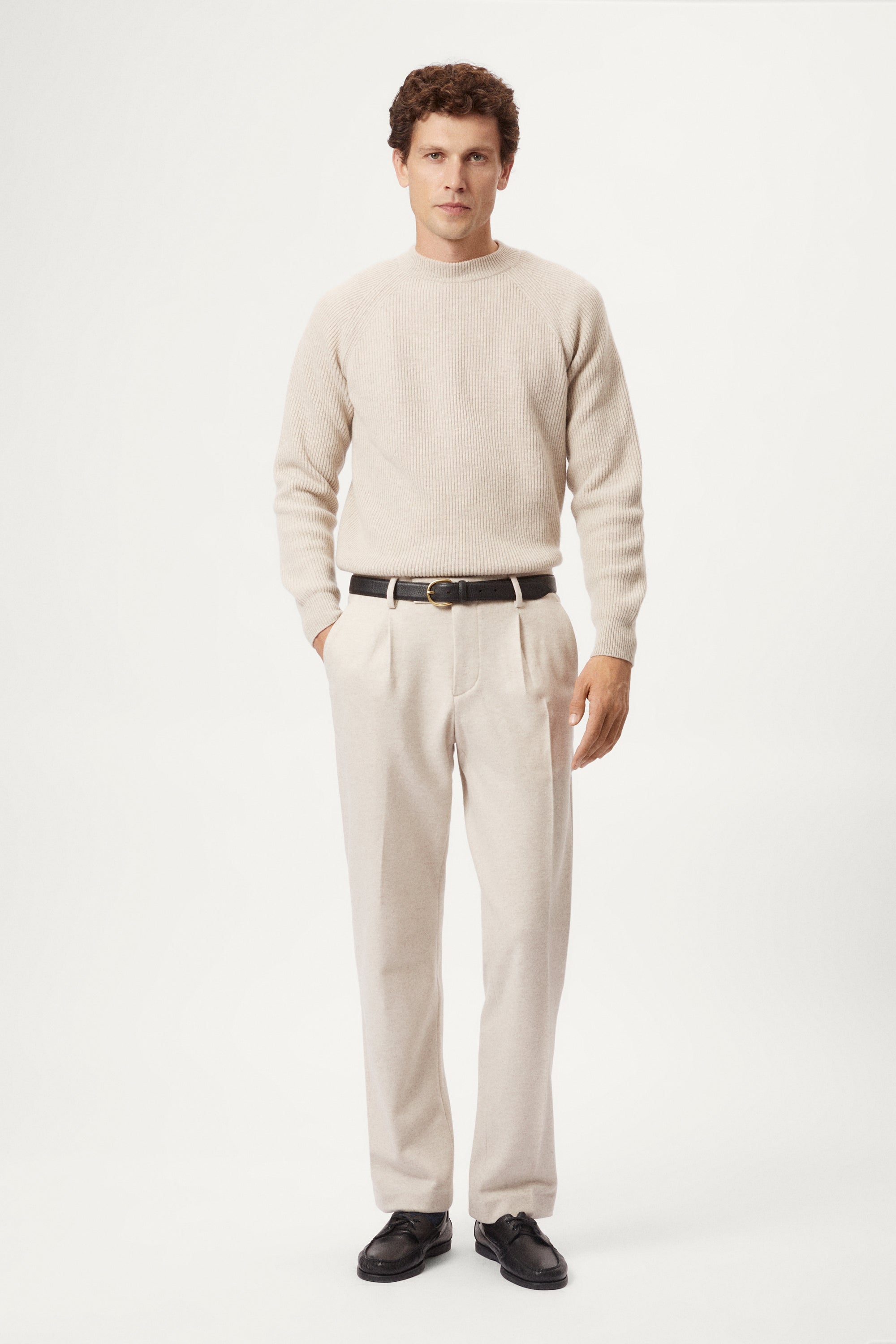 Person wearing a woolen beige pants and a light sweater on a white background